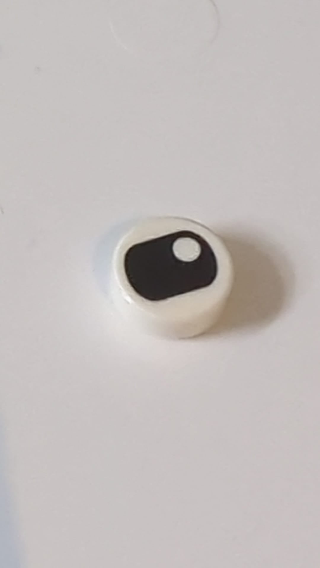 1x1 Fliese rund mit schwarzem, zusammengekniffenem Auge und vertikal zentrierter Pupille weiß