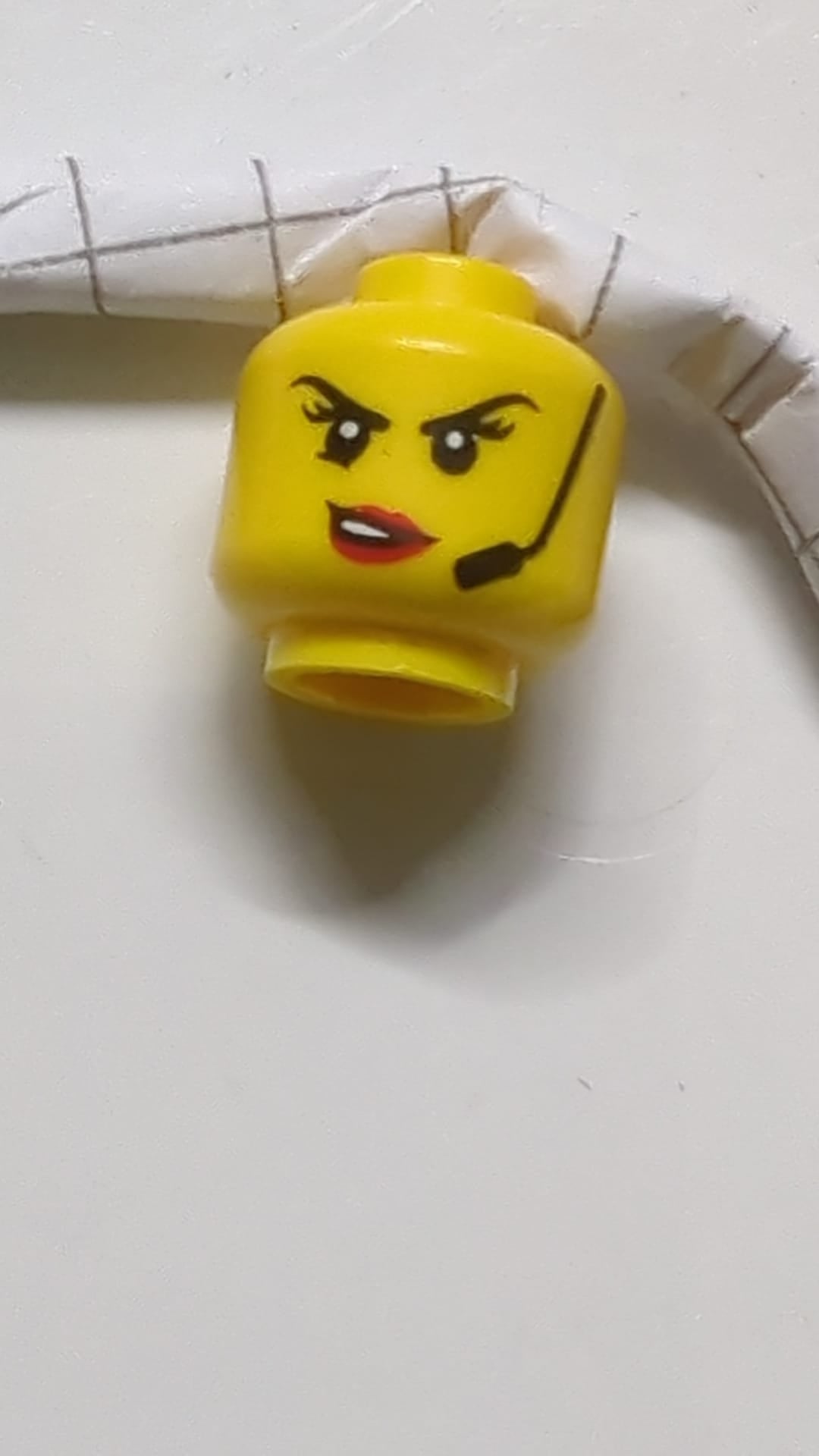 Minifigur, weiblicher Kopf mit schwarzen Augenbrauen, Headset, roten Lippen mit offenem Mund und schiefem Lächeln/grimmigem Gesichtsausdruck gelb