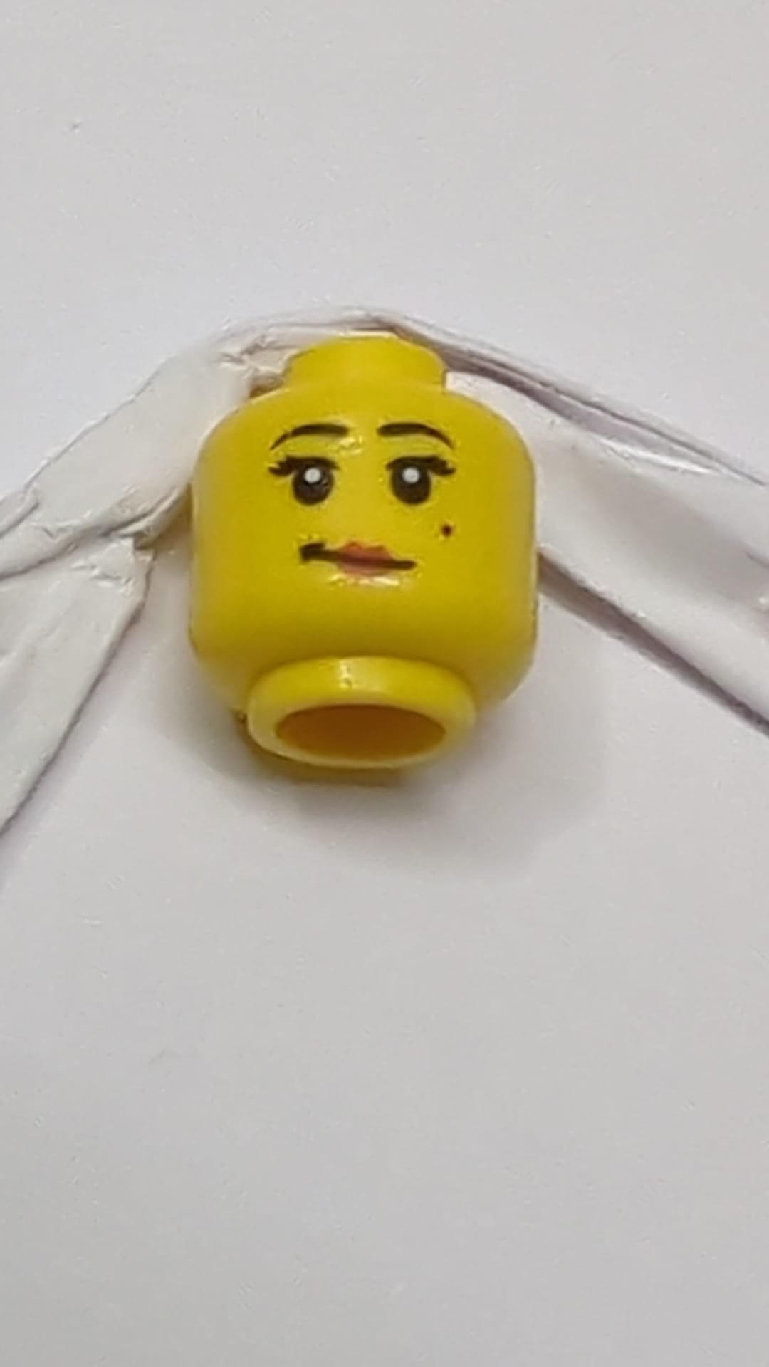 Minifigur, weiblicher Kopf, schwarze Augenbrauen, Wimpern und Schönheitsfleck, rote Lippen, schiefes Grinsen gelb