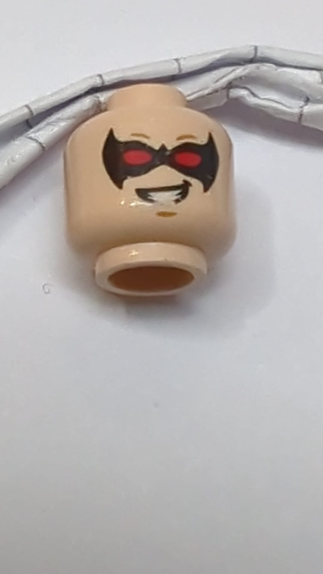 Minifigur, Kopf: Doppelseitiger männlicher Kopf mit schwarzer, spitzer Augenmaske und roten Augen, mittelgroßes nougatfarbenes Grübchen am Kinn, entschlossenes/schiefes Lächeln mit Zähnen hellnougat (fleischfarben)