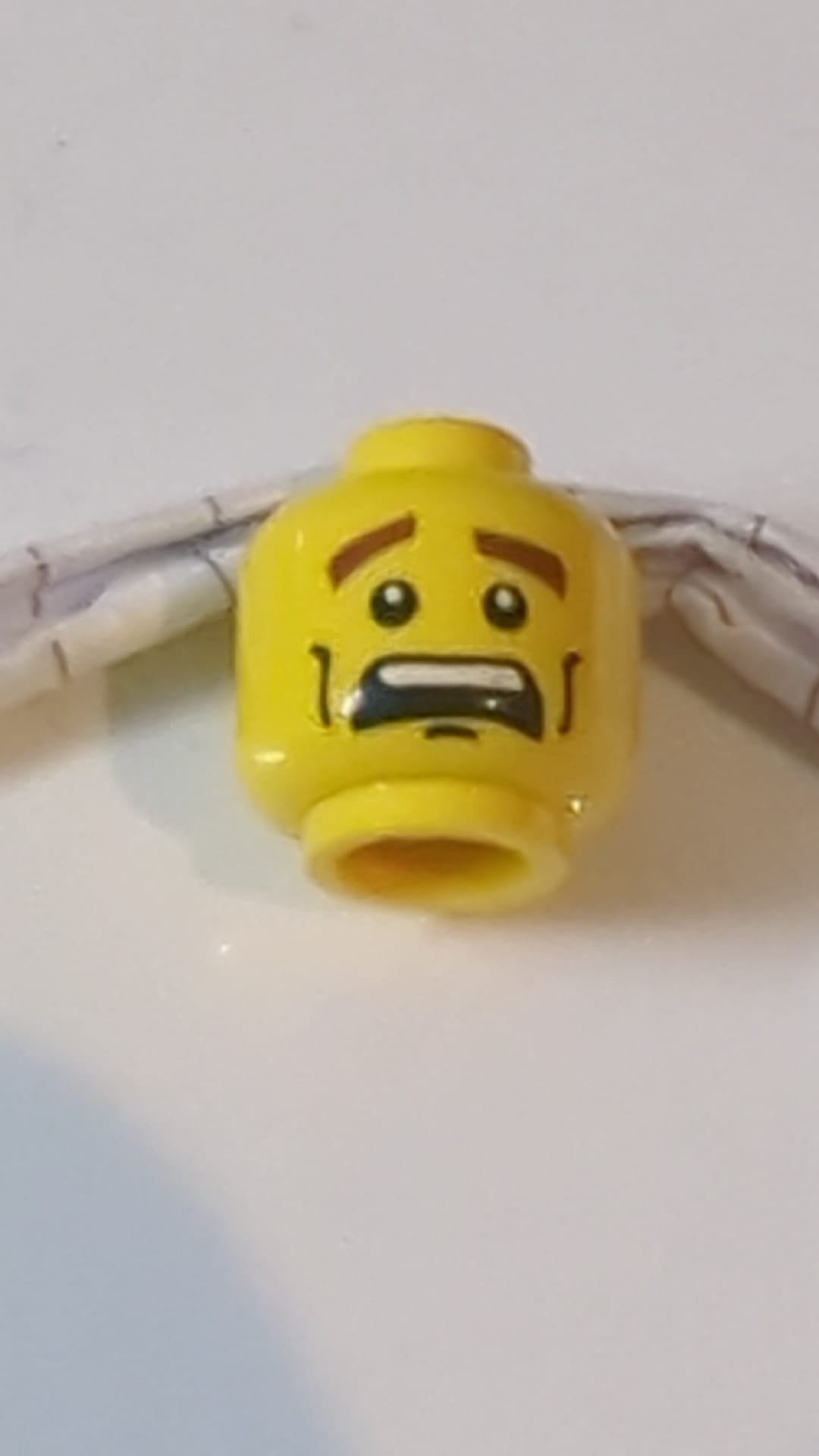 Minifigur, Kopf doppelseitig, rötlich-braune, dichte Augenbrauen, schwarze Wangenfalten und Grübchen am Kinn, ängstlicher, offener Mund mit sichtbaren oberen Zähnen / strenges Gesichtsmuster gelb