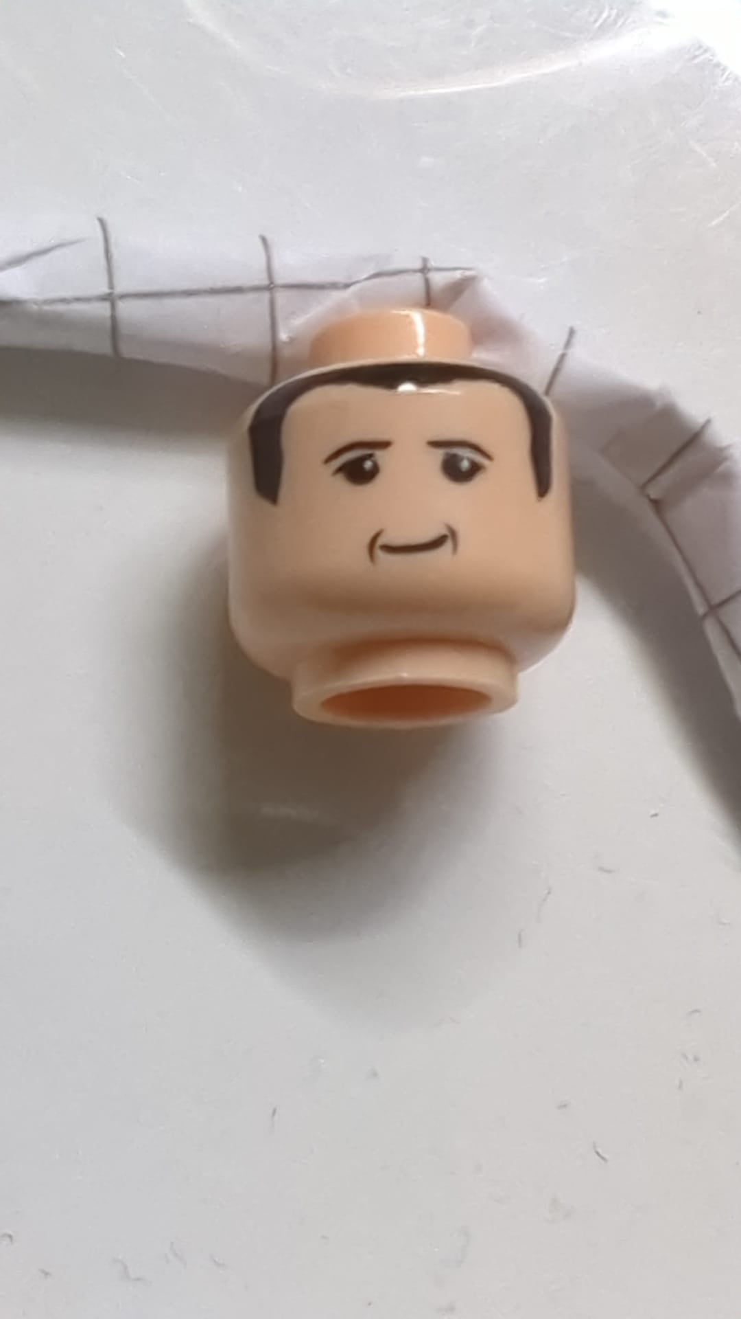 Minifigur, Kopf: Schwarze, kleine, dünne Augenbrauen, Oberlider, Wangenfalten und Haare, schiefes Grinsen hellnougat (fleischfarben)