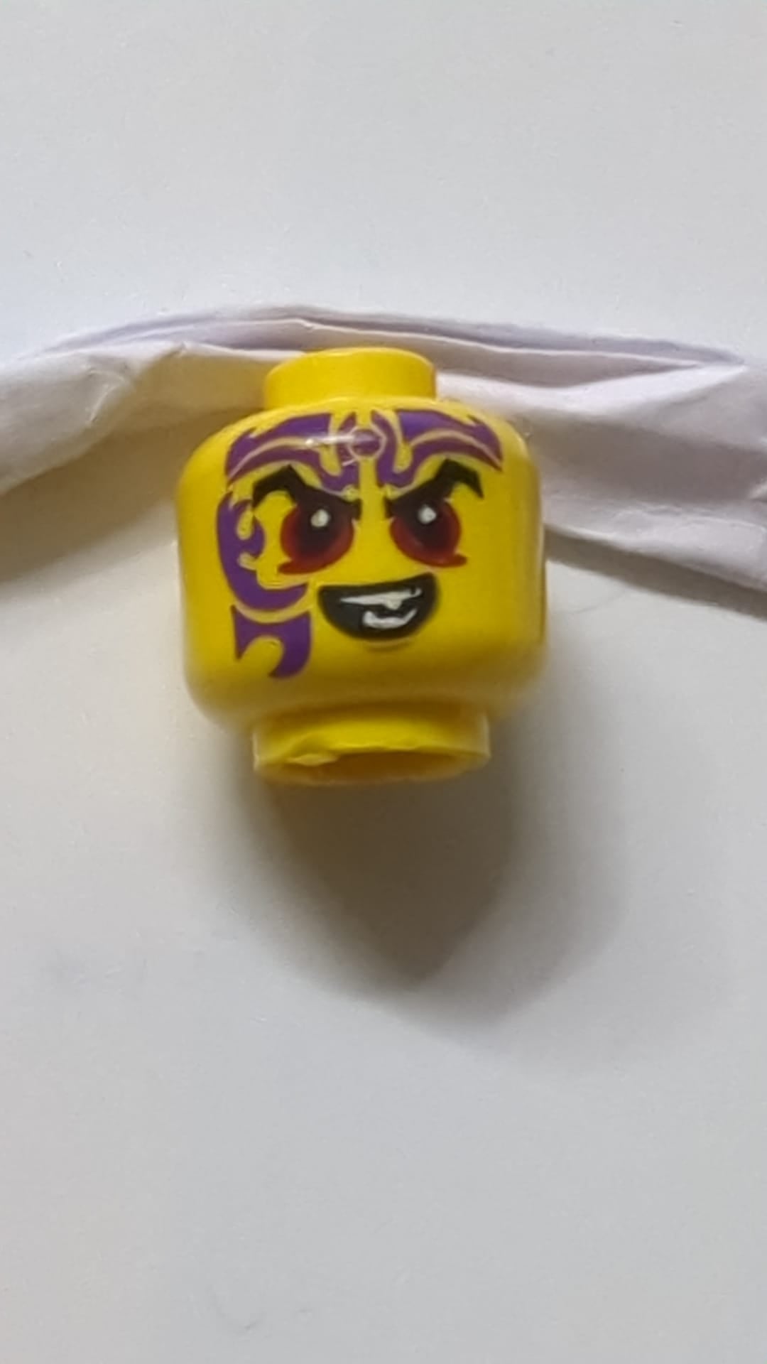 Minifigur, Kopf, schwarze Augenbrauen, dunkelrote Augen, dunkelviolettes Tattoo, Muster eines bösen Lächelns gelb