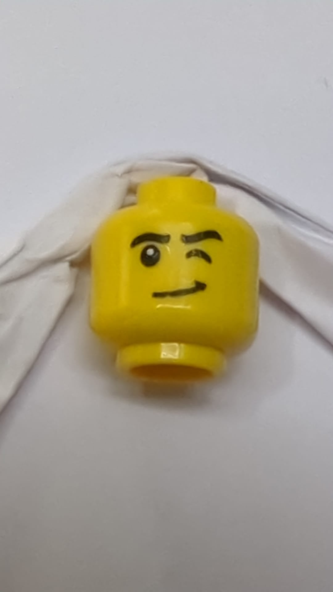 Minifigur, Kopf: schwarze Augenbrauen, linkes Auge zwinkert, schiefes Grinsen mit Grübchenmuster gelb