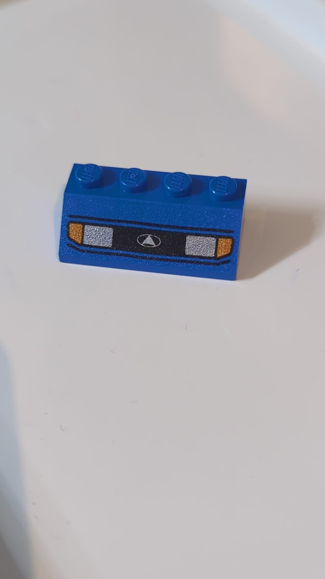 2x4 Dachstein 45° mit silbernen Autoscheinwerfern, orangefarbenen Blinkern und schwarzem Kühlergrill mit weißem Dreieck-im-Oval-Logo blau