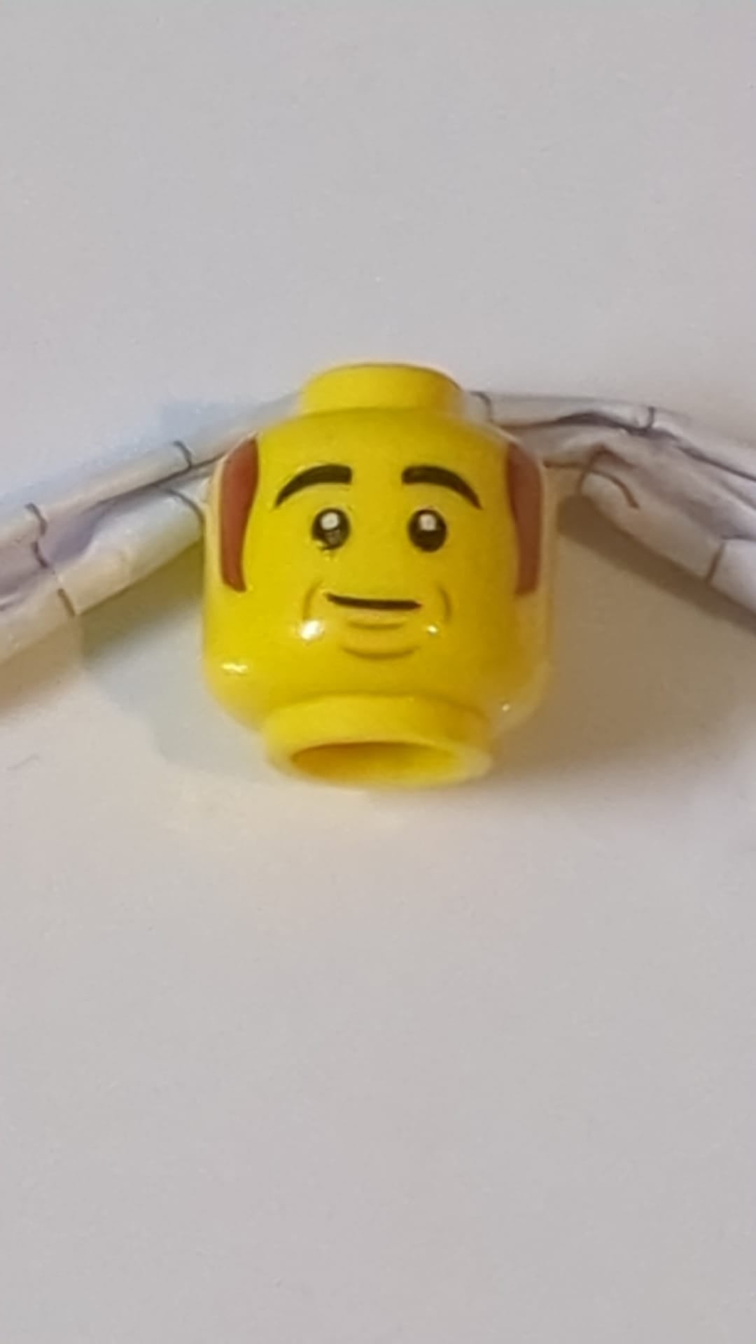 Minifigur, Kopf: Schwarze, dichte Augenbrauen, rötlich-braune Koteletten, Wangenfalten, Grübchen am Kinn, schiefes Grinsen gelb