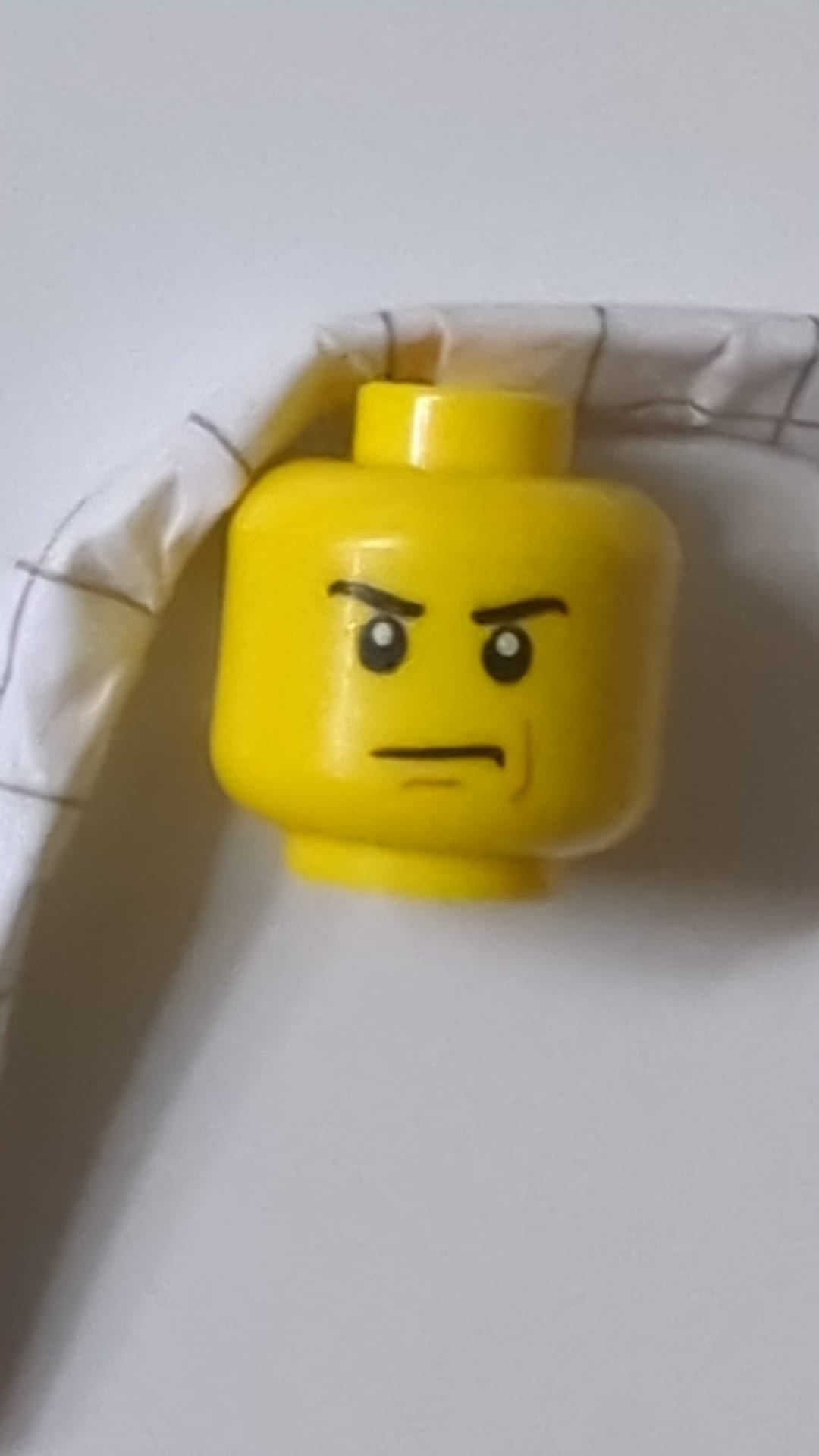 Minifigur, männlicher Kopf mit wütend zusammengezogenen Augenbrauen und finsterem Blick, rotbraunes Linienmuster auf der linken Wange gelb