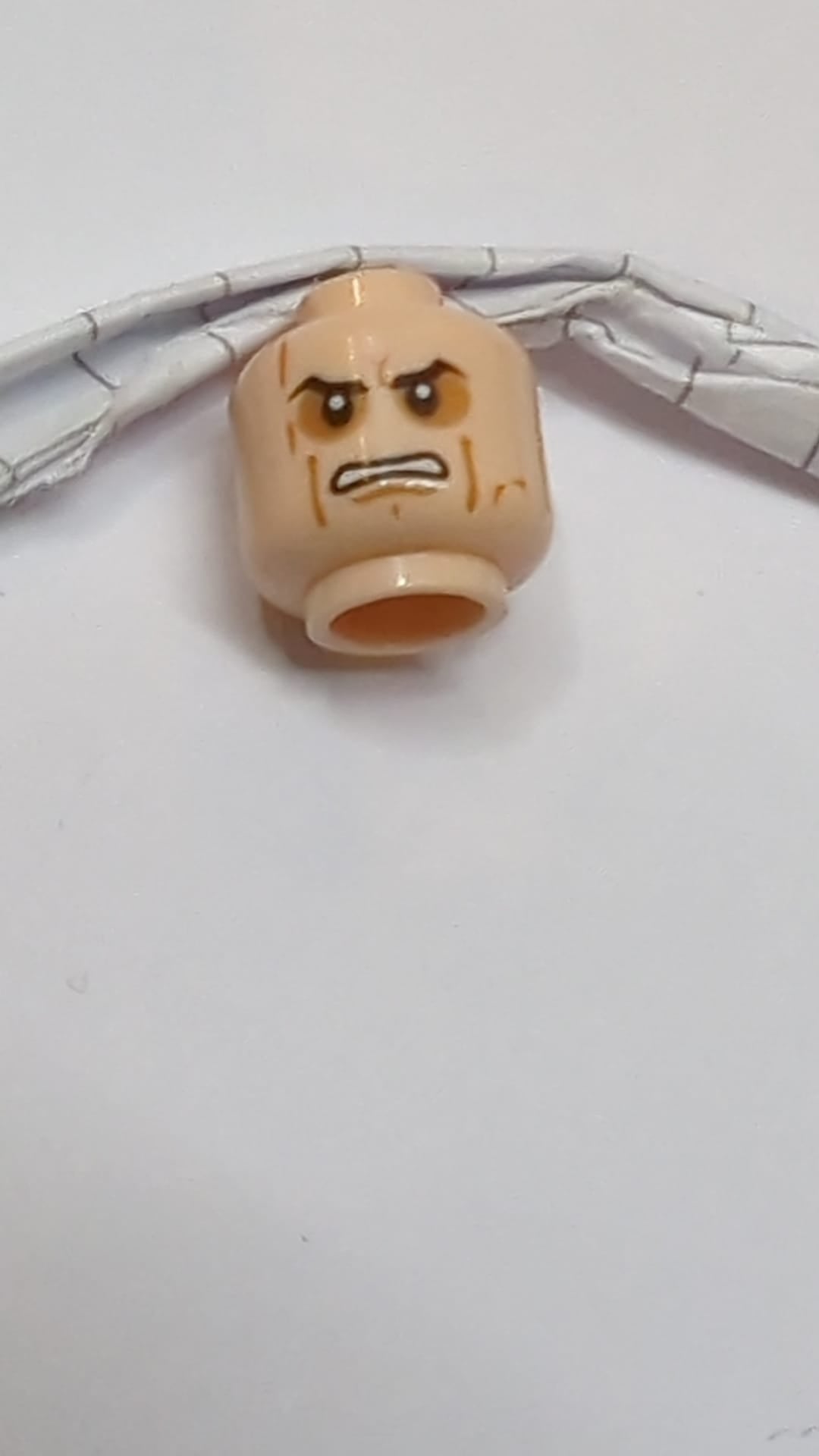 Minifigur, Kopf: Doppelseitig schwarz, schräge Augenbrauen, dunkelorangefarbener Lidschatten, Wangenfalten, Grübchen und Narben am Kinn, wütend geöffneter Mund mit Zähnen / gelbe Augen und strenges Muster hellnougat (fleischfarben)