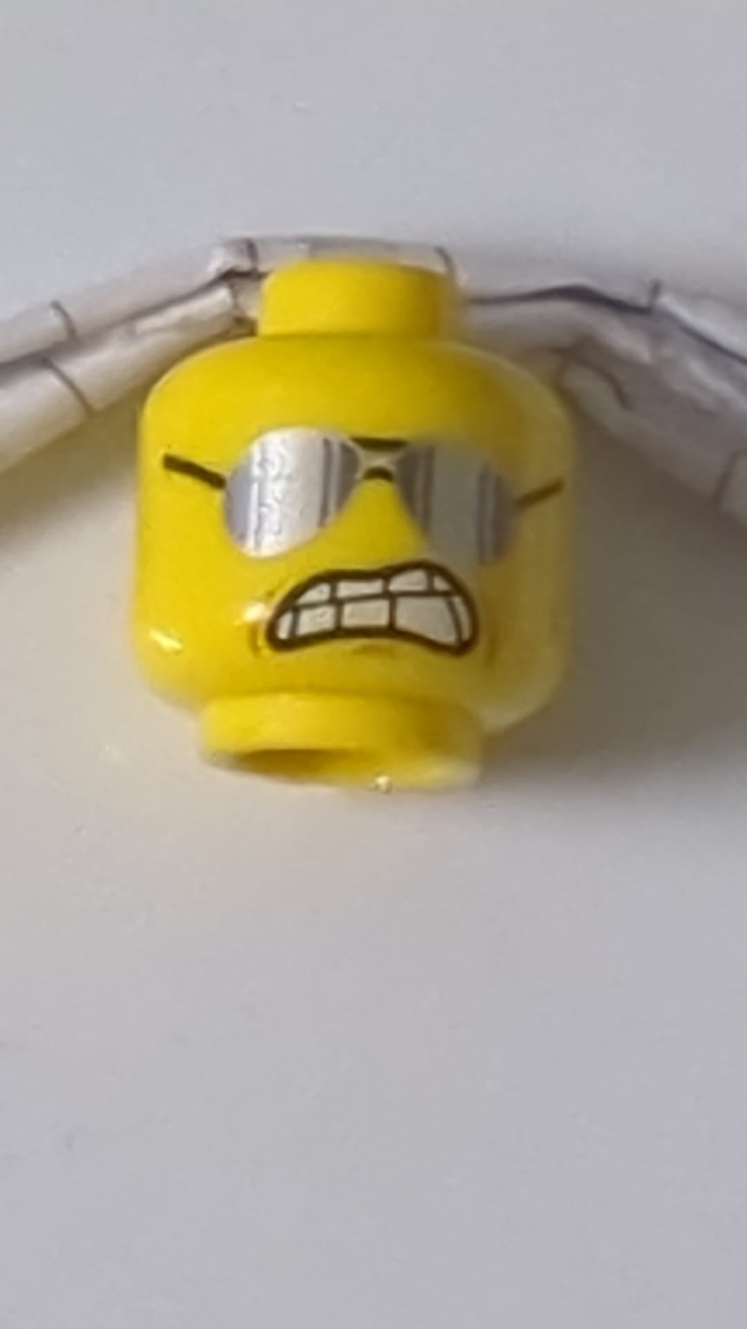 Minifigur, Kopf mit doppelseitiger schwarzer Brille, offenes Lächeln mit Zähnen und Zunge / Sonnenbrille, zusammengebissene Zähne gelb