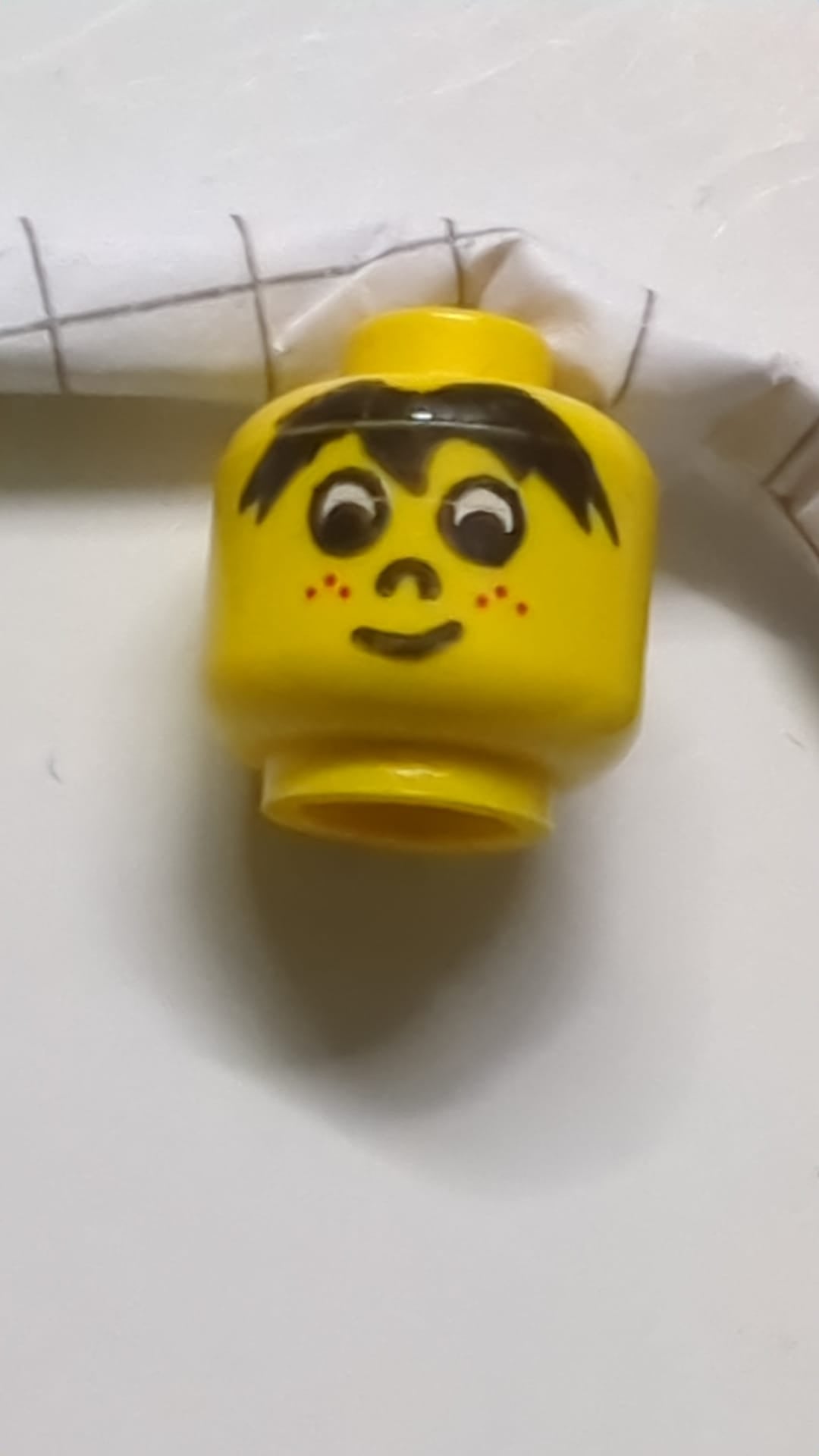 Minifigur, Kopf: schwarze Haare, weiße Augen, Nase, rote Sommersprossen, schiefes Grinsen gelb
