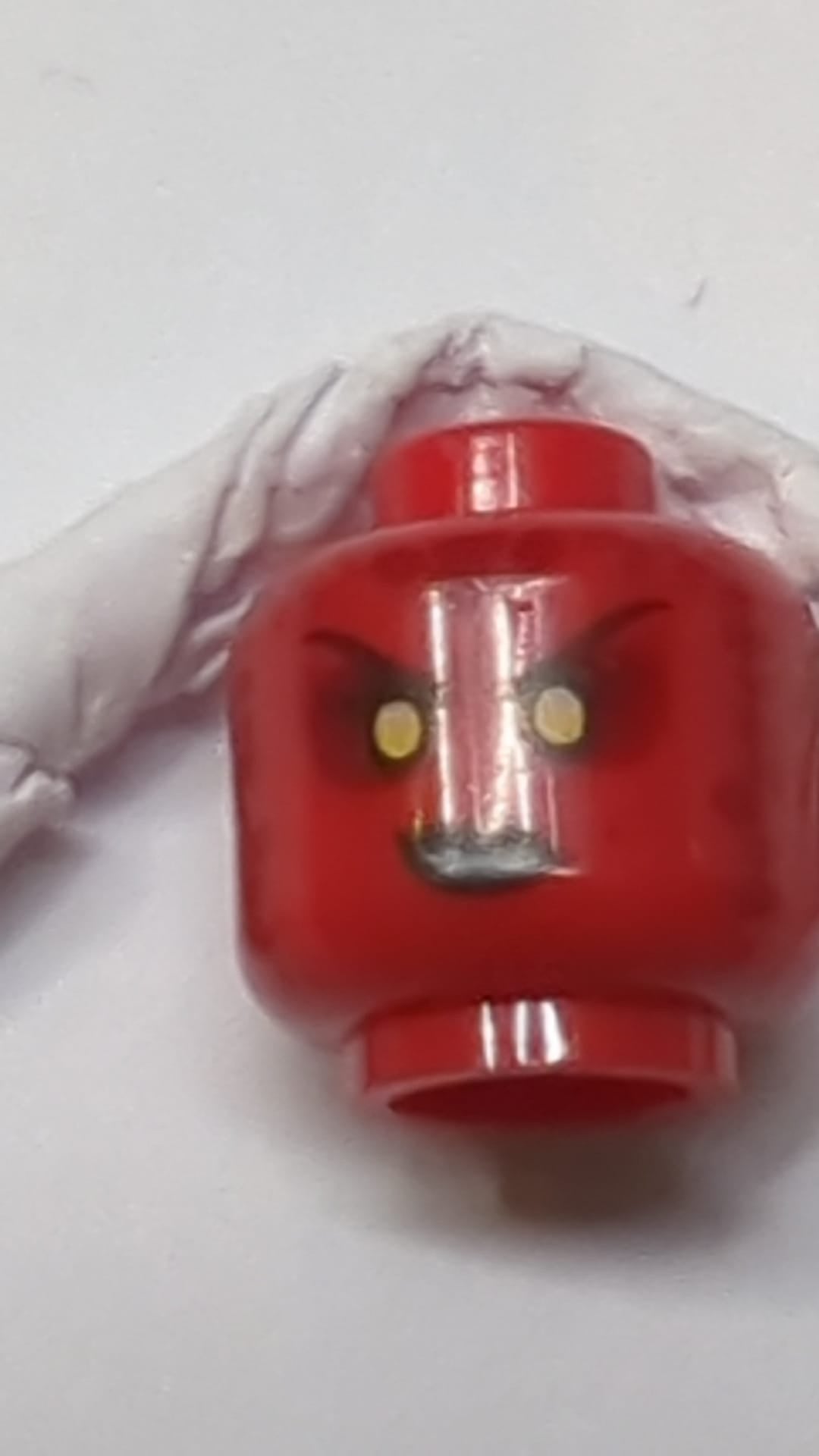 Minifigur, doppelseitiger Kopf eines Alien-Lava-Monsters mit schwarzen Augenbrauen, gelben Augen, dunkelrotem Lidschatten und Flecken, schwarzem Lippenstift und einem grinsenden/gefletschten Zähnen rot