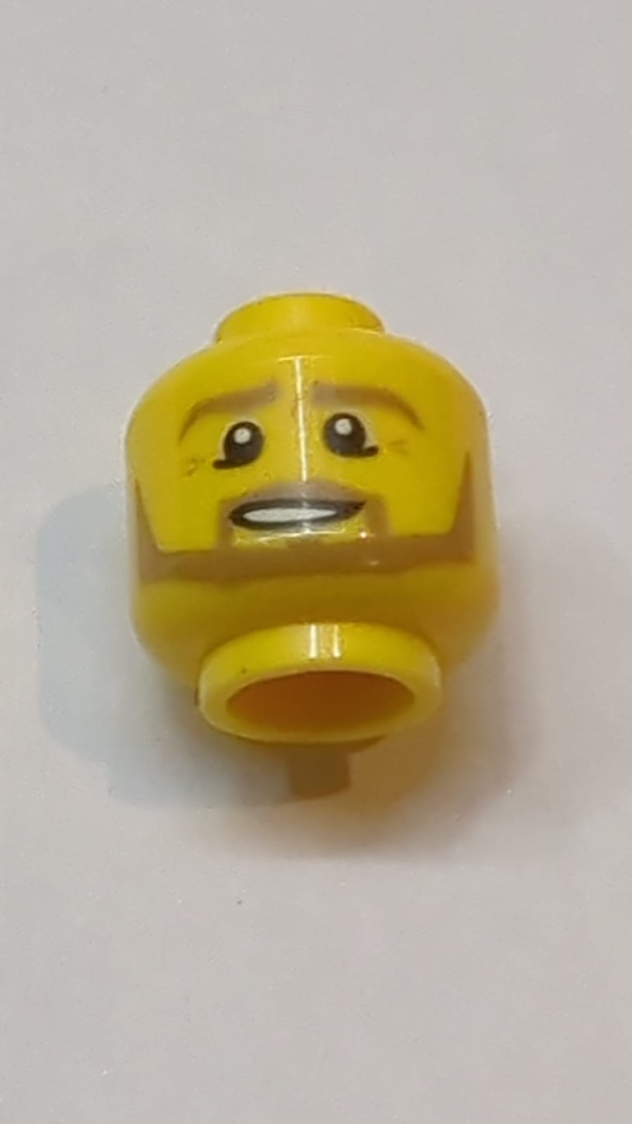 Kopf mit dunkelbraunen Augenbrauen, Schnurrbart und kantigem Bart, Unterlider, mittlere Nougat-Falten, schiefes offenes Mundlächeln mit Zähnen und Linienmuster der Oberlippe