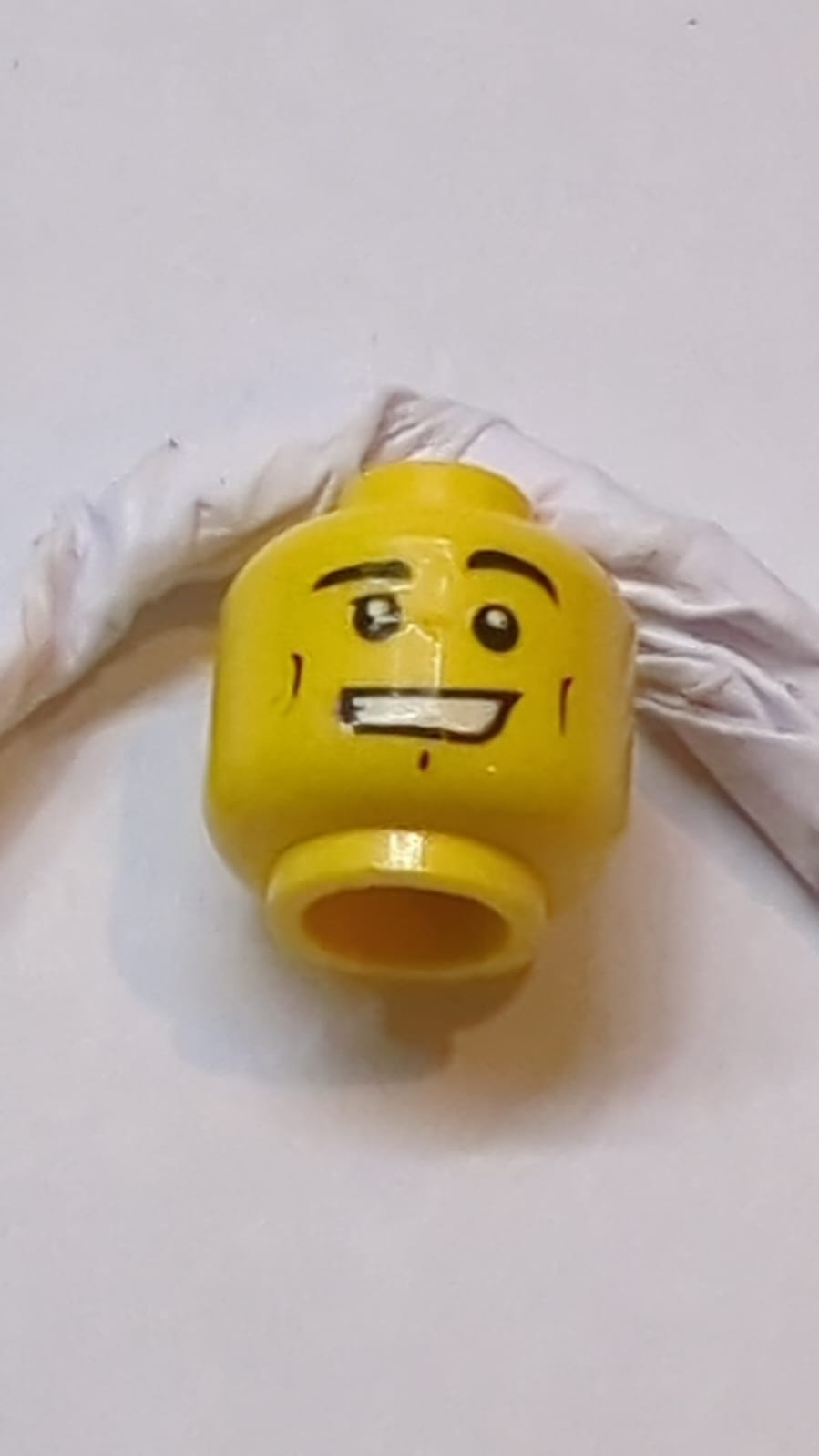 Kopf, schwarze Augenbrauen, links hochgezogen, kleine Wangenlinien, Grübchen am Kinn, offenes Lächeln mit sichtbaren Zähnen