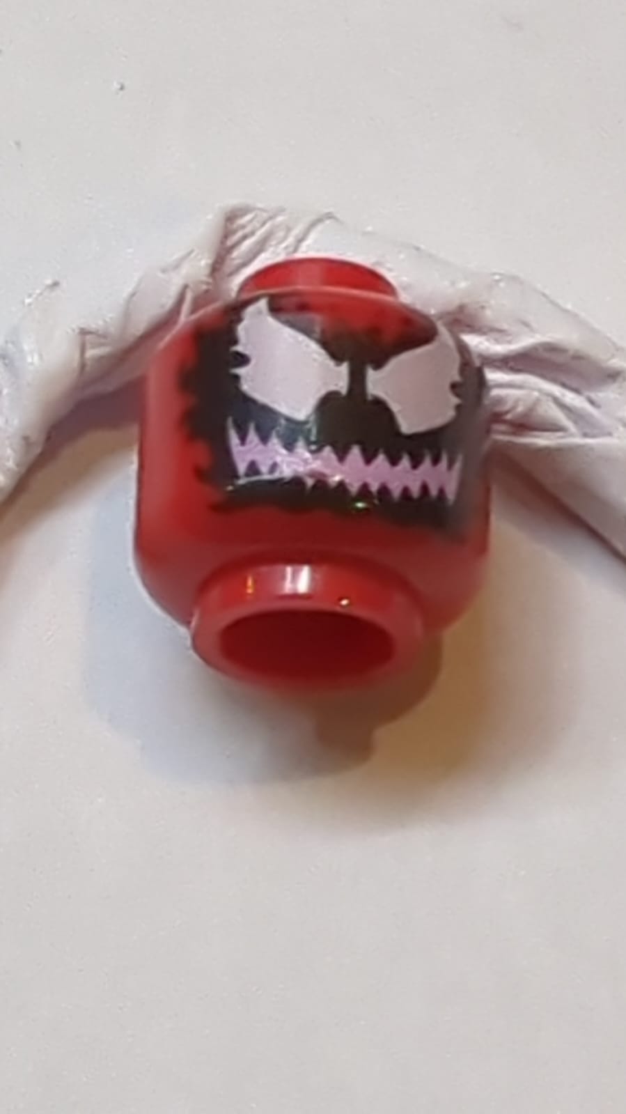 Kopf Außerirdischer mit großen weißen Augen und breitem, leuchtend pinkem Grinsen mit scharfen Zähnen auf schwarzem Muster (Carnage)