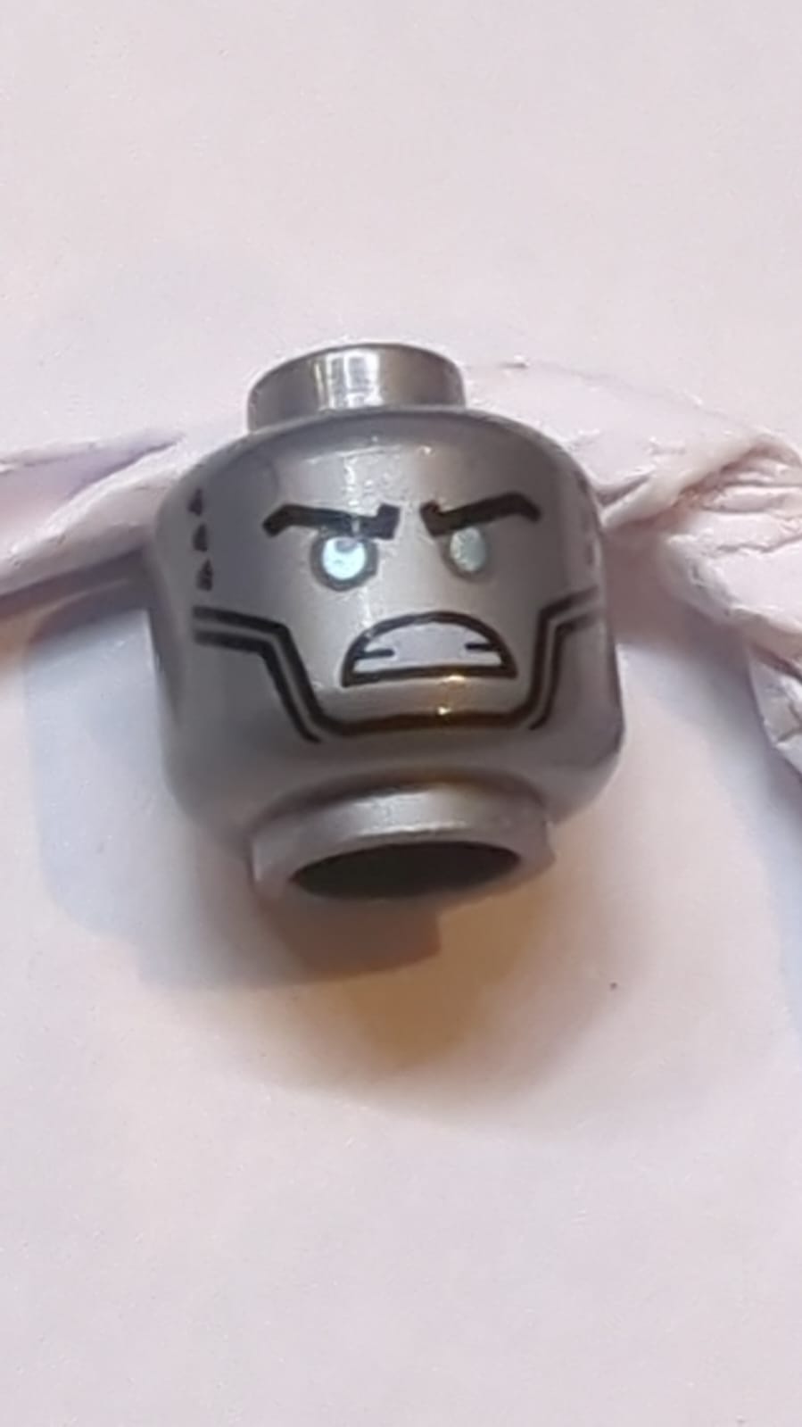 Kopf Außerirdischer Roboter mit schwarzen Augenbrauen, metallisch hellblauen Augen, Wangenlinien, wütend gebleckten Zähnen, Lüftungsschlitzen und silbernem Kreis auf dem Rückenmuster