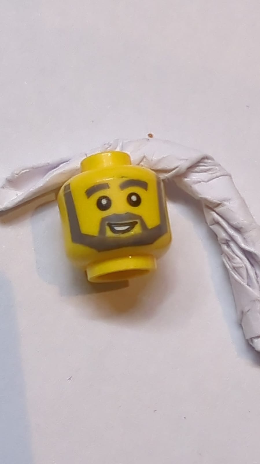 Kopf Dunkelbläulich graue, dicke Augenbrauen, kantiger Bart und dicke Koteletten, schief lachender Mund mit offenem Mund und weißen Zähnen