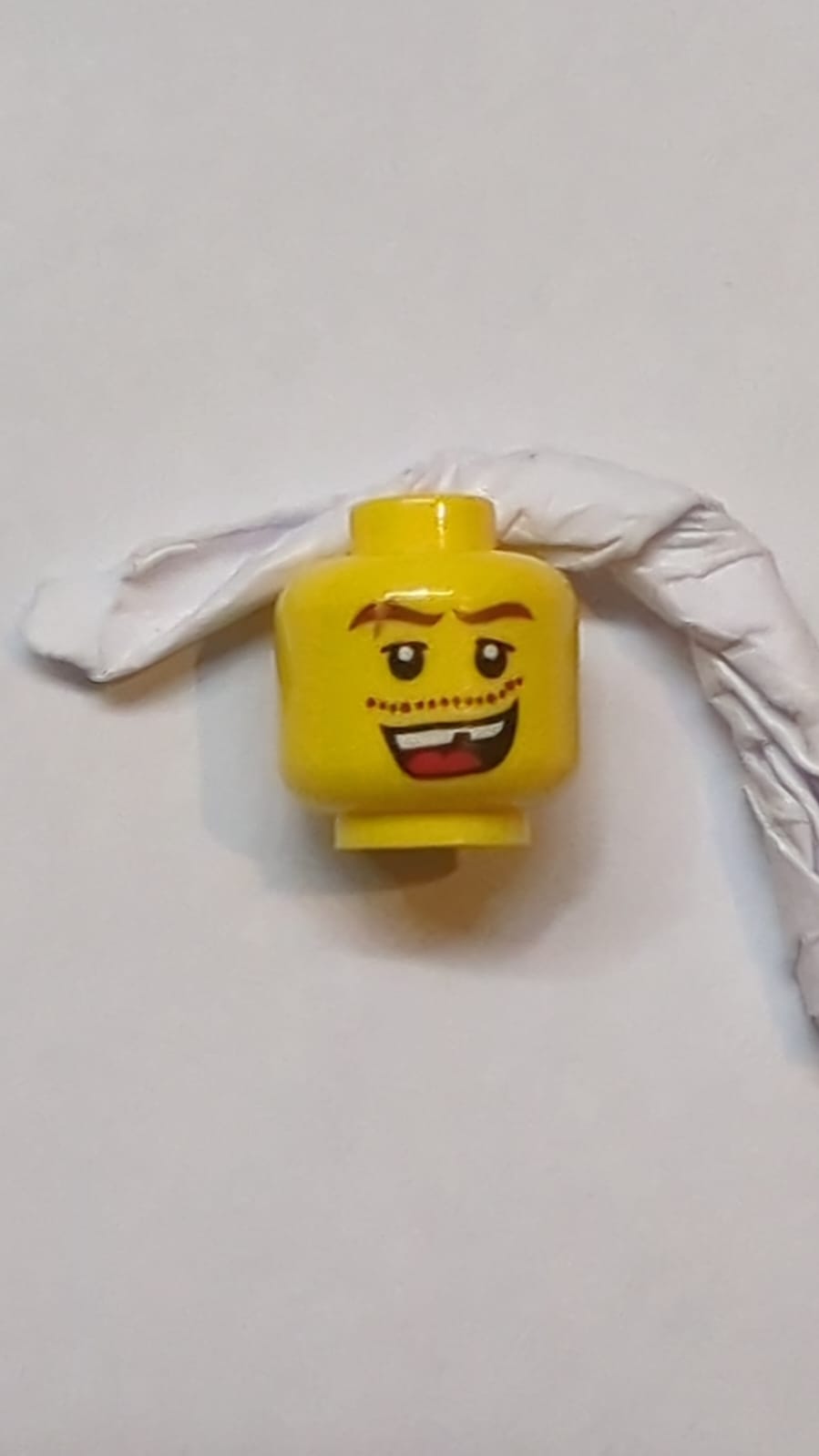 Kopf Rötlich-braune, wellige Augenbrauen mit Narbe, obere Augenlider, Schnurrbartstoppeln, offenes Mundlächeln mit oberen Zähnen und roter Zunge, fehlendes Zahnmuster