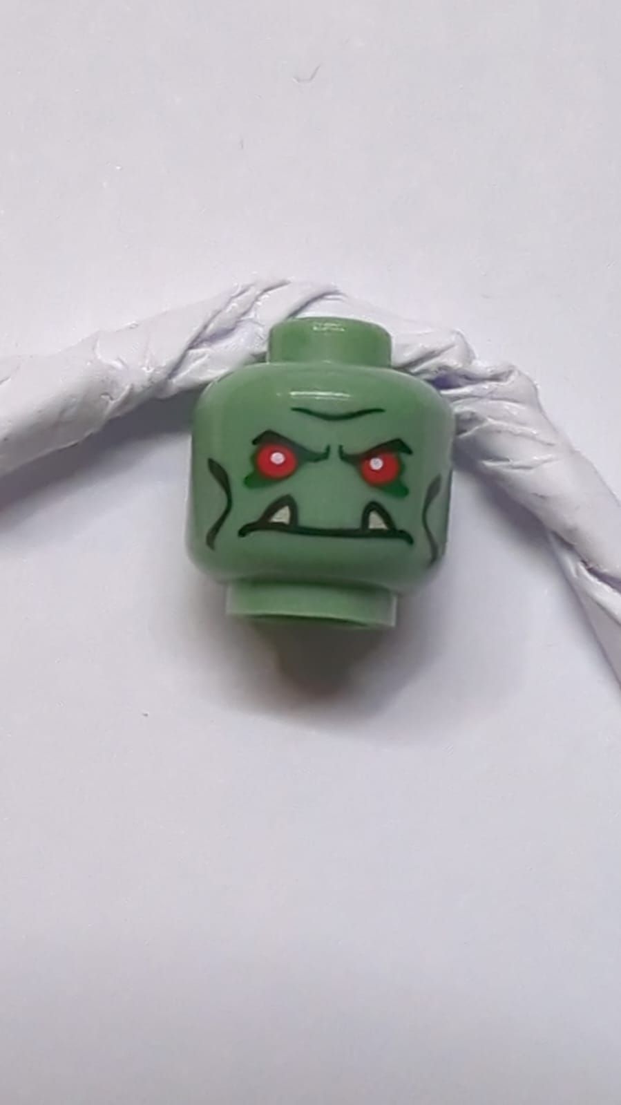 Kopf eines Alien-Trolls mit roten Augen, schwarzen Augenbrauen und Wangenlinien, dunkelgrünem Lidschatten und Stirnrunzeln mit Muster aus beigefarbenen unteren Fangzähnen sandgrün