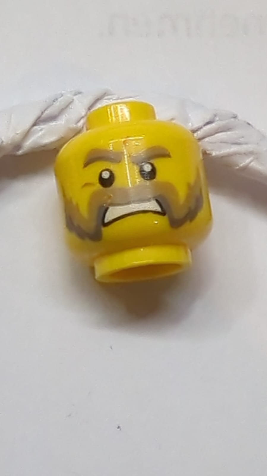 Kopf dunkelbraun und dunkel bläulich-graue dicke Augenbrauen, Schnurrbart und Koteletten, mittelbraune Nasenfalten, wütend geöffneter Mund mit Zähne-Muster gelb