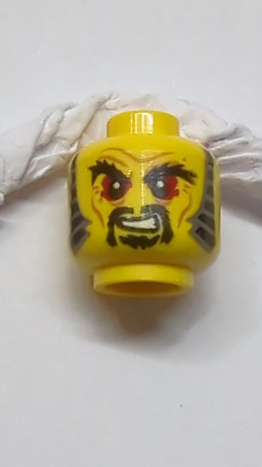 Kopf mit schwarzen buschigen Augenbrauen, roten Augen, Schnurrbart und Kinnbart, Koteletten, Faltenmuster gelb