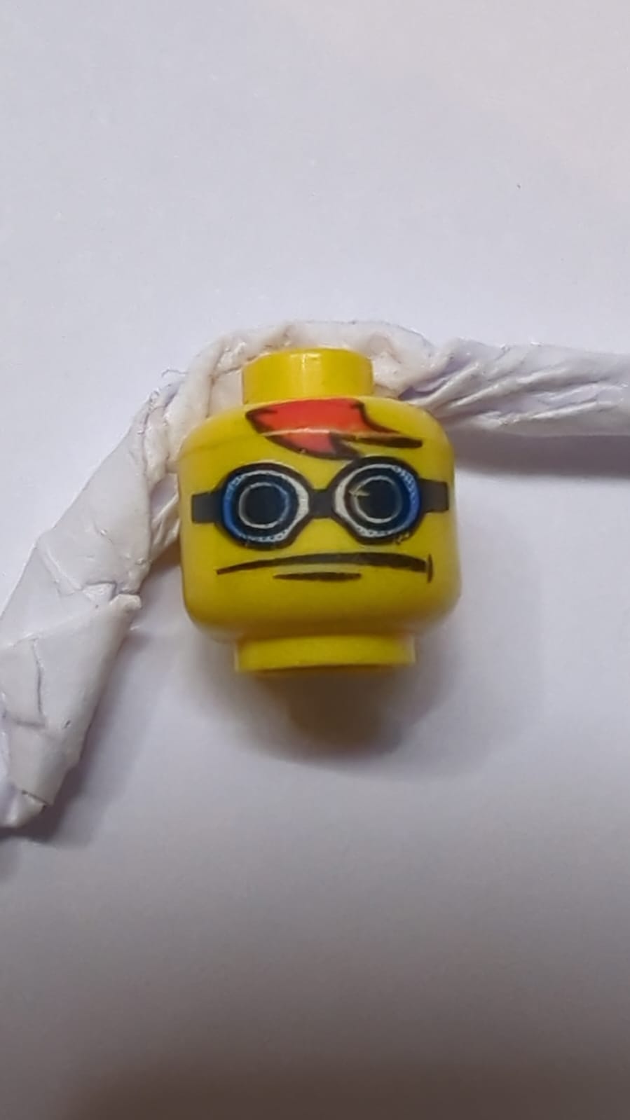 Kopf mit blauen und weißen Schutzbrillen mit schwarzem Riemen, roten Haarfransen, Grübchen am Kinn, breites neutrales Muster gelb