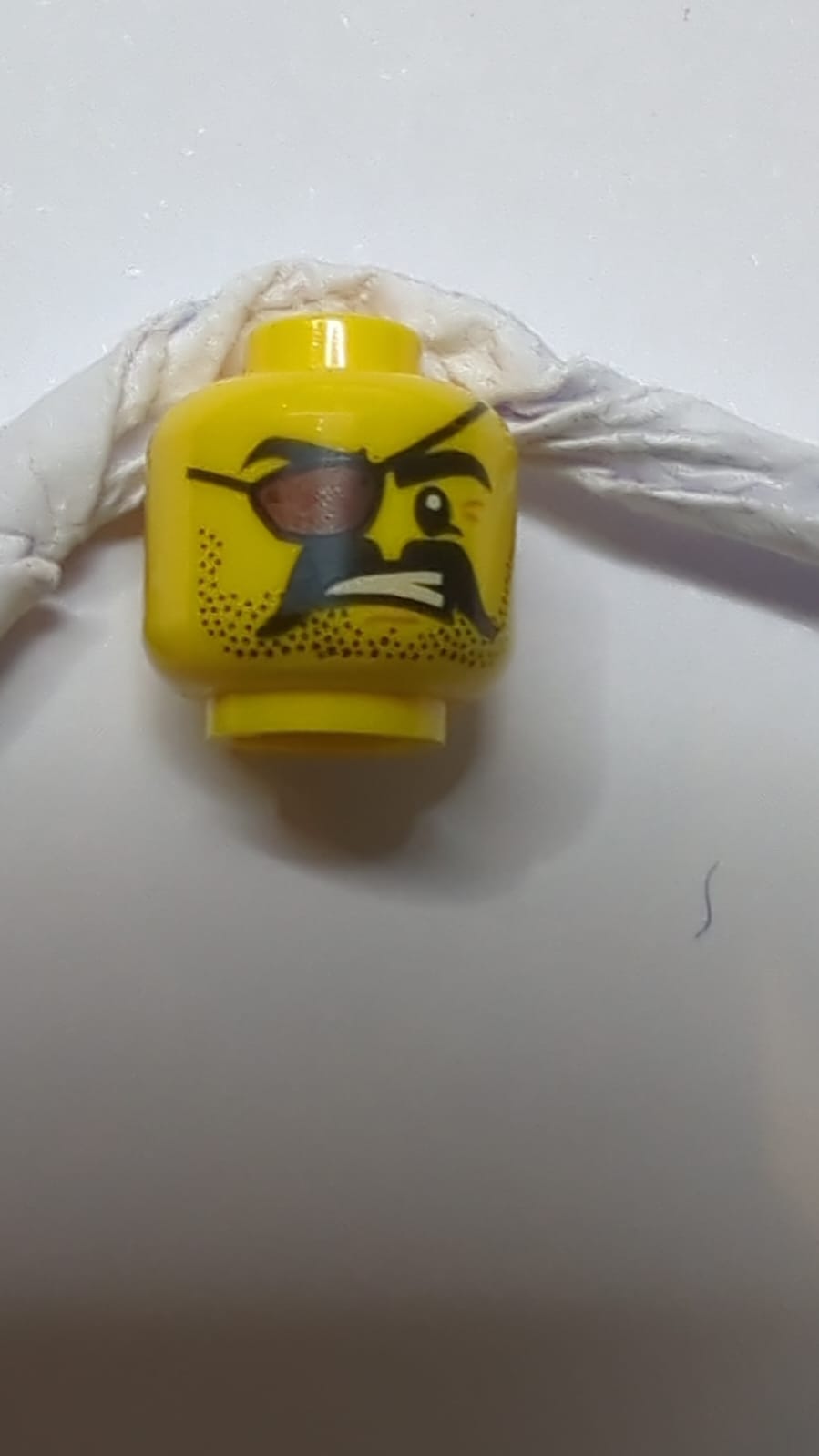 Kopf mit schwarzem Stoppelbart und Schnurrbart, Augenklappe, Krähenfüße, entblößtes Zähne-Muster gelb