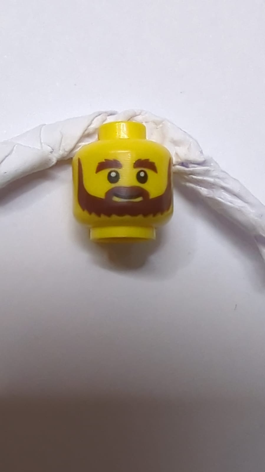 Kopf mit braunem Bart, buschigen Augenbrauen, Grinsen und weißen Pupillenmuster gelb