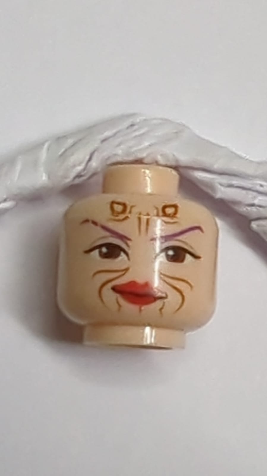 Minifigur, Kopf eines Außerirdischen mit dunkelvioletten dünnen Augenbrauen, großen rötlich-braunen Augen, Hörnern und Markierungen, roten Lippen, Grinsen, Pferdeschwanz auf der Rückenmuster nougat (hell)