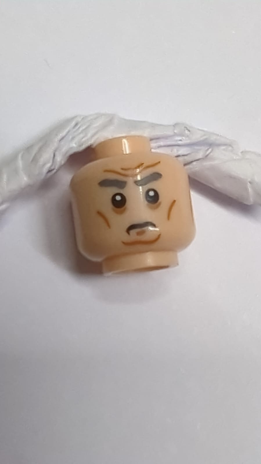 Minifigur, Kopf dunkelblaugrau, buschige Augenbrauen, mittlere Nougatrötung an den Wangen, Grübchen im Kinn und Falten, zusammengezogene Augenbrauen, ernstes Muster nougat (hell)