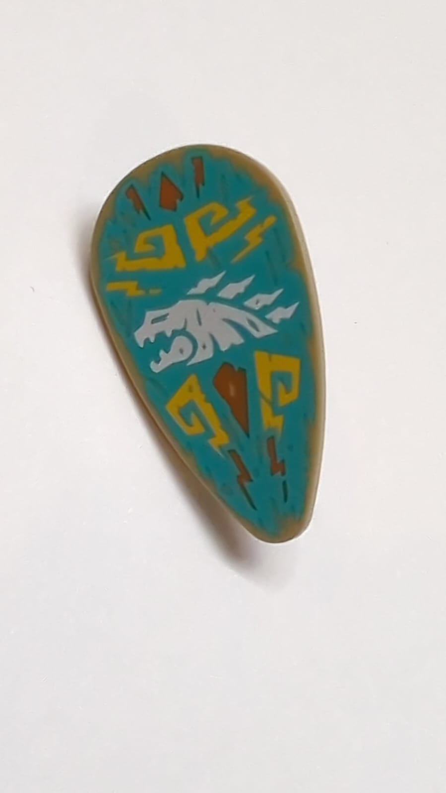 Minifigur, Schild oval mit weißem Drachenkopf und hellorangefarbener Filigran auf dunkeltürkisfarbenem Hintergrundmuster dunkelbeige