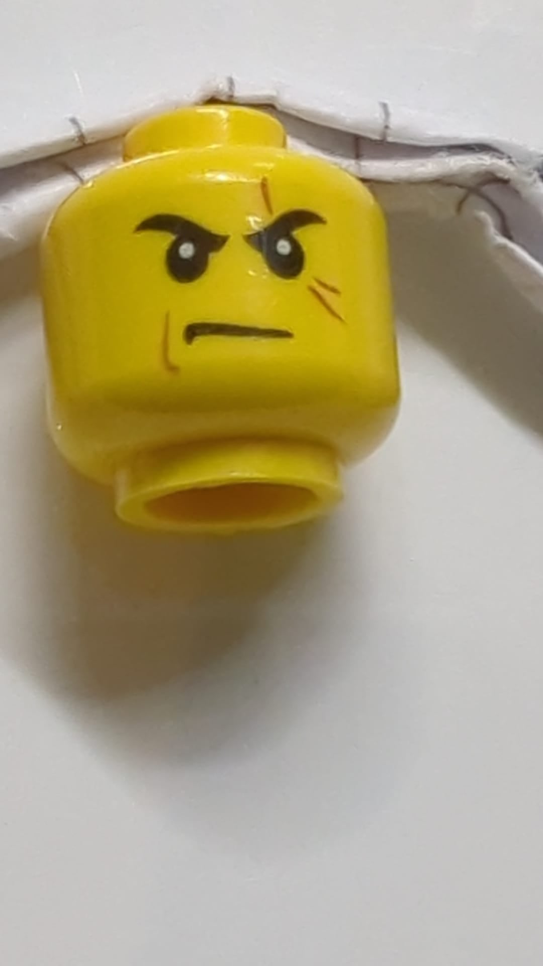 Minifigur, Kopf: Schwarze Augenbrauen, dunkelorangefarbene Narbe über dem linken Auge, mittelbraune Wangenlinie, finsterer Gesichtsausdruck gelb