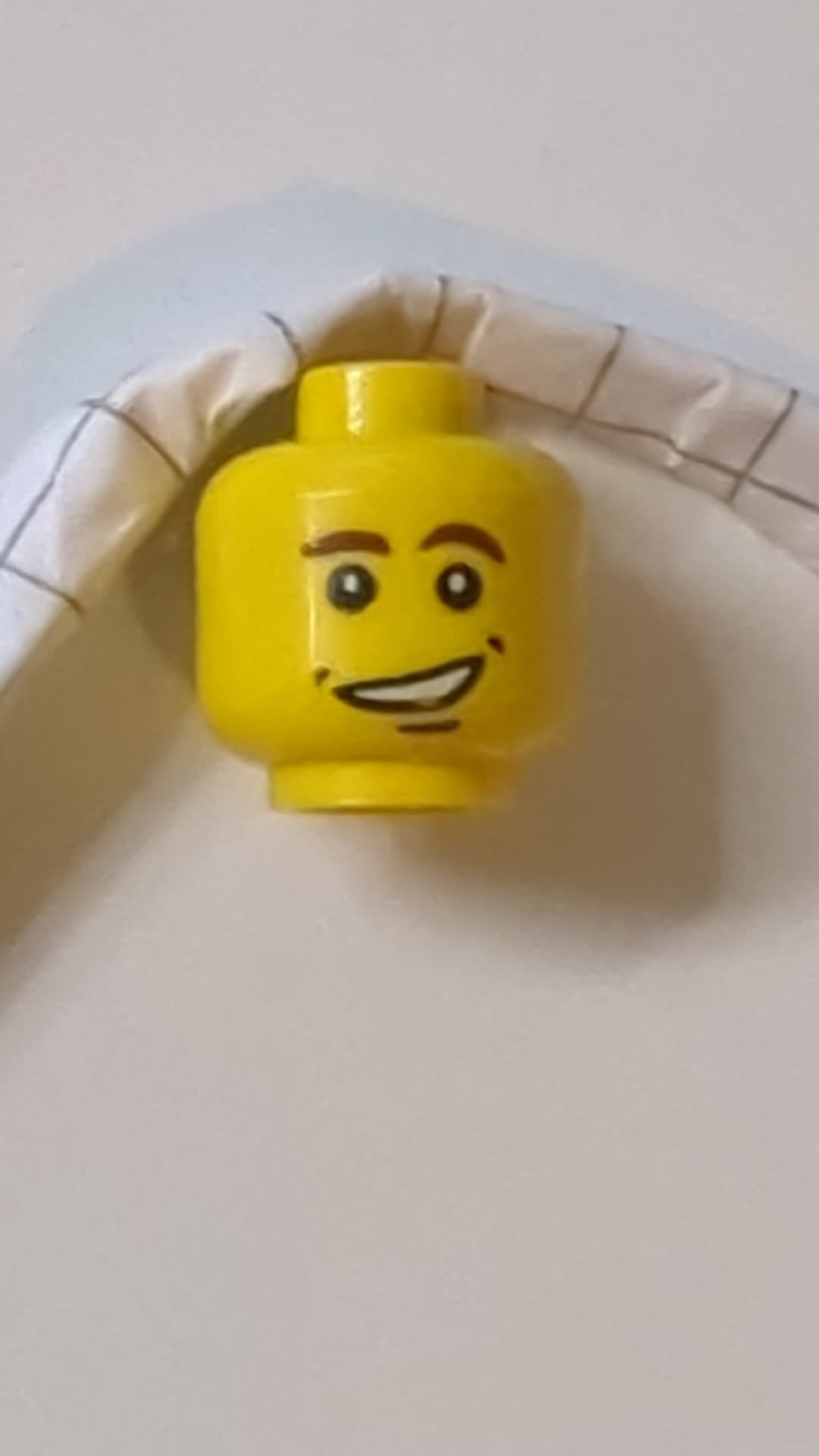 Minifigur, rötlich-brauner Kopf, dichte Augenbrauen, Grübchen und Kinngrübchen, schiefes, offenes Lächeln mit Zahnmuster gelb