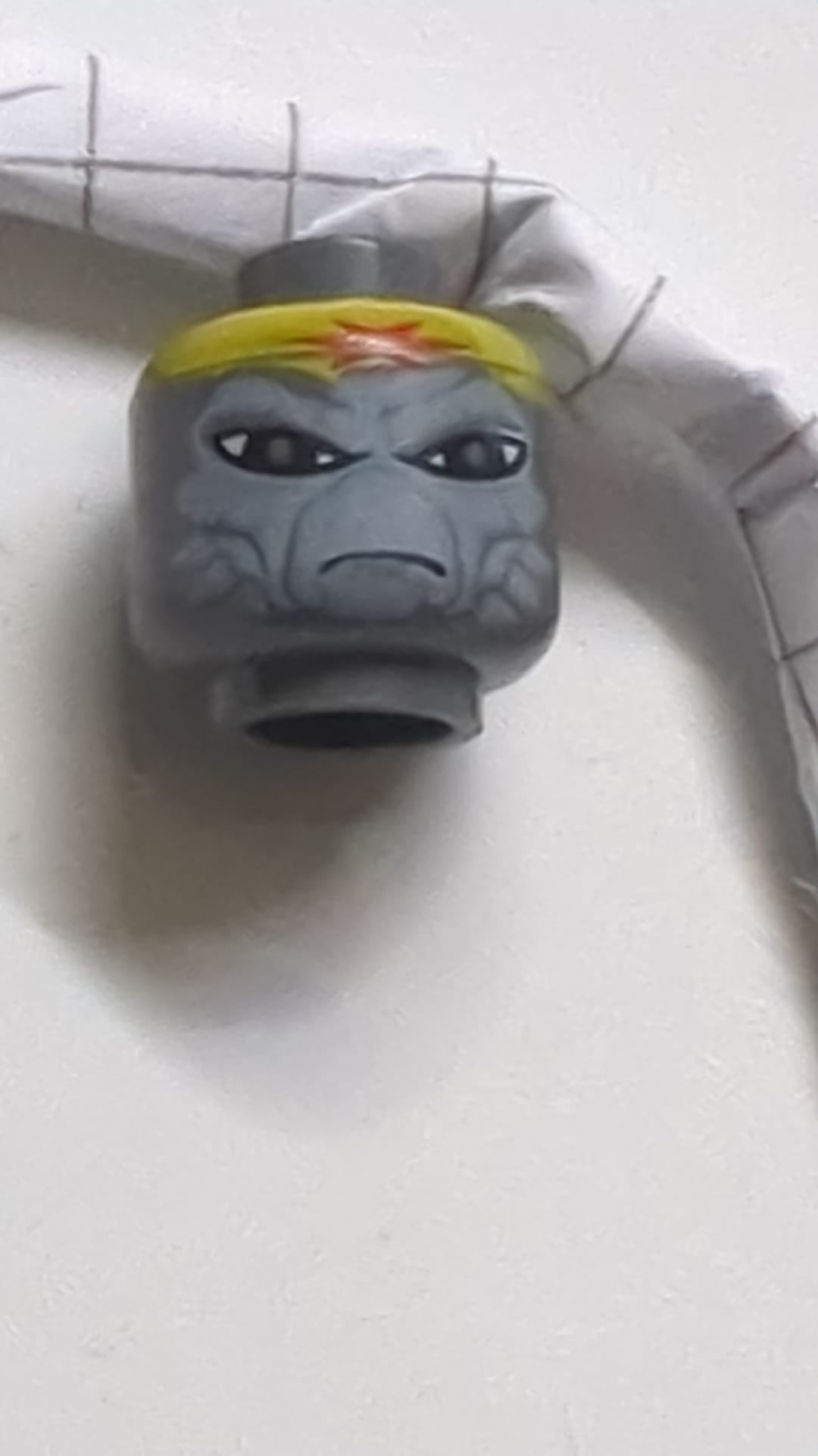 Minifigur, Kopf Alien SW Weequay mit hellblaugrauem Gesicht, großen schwarzen Augen, gelbem Bandana mit rotem Stern, finsterem Blick und Pferdeschwanz mit Band am Hinterkopf neudunkelgrau