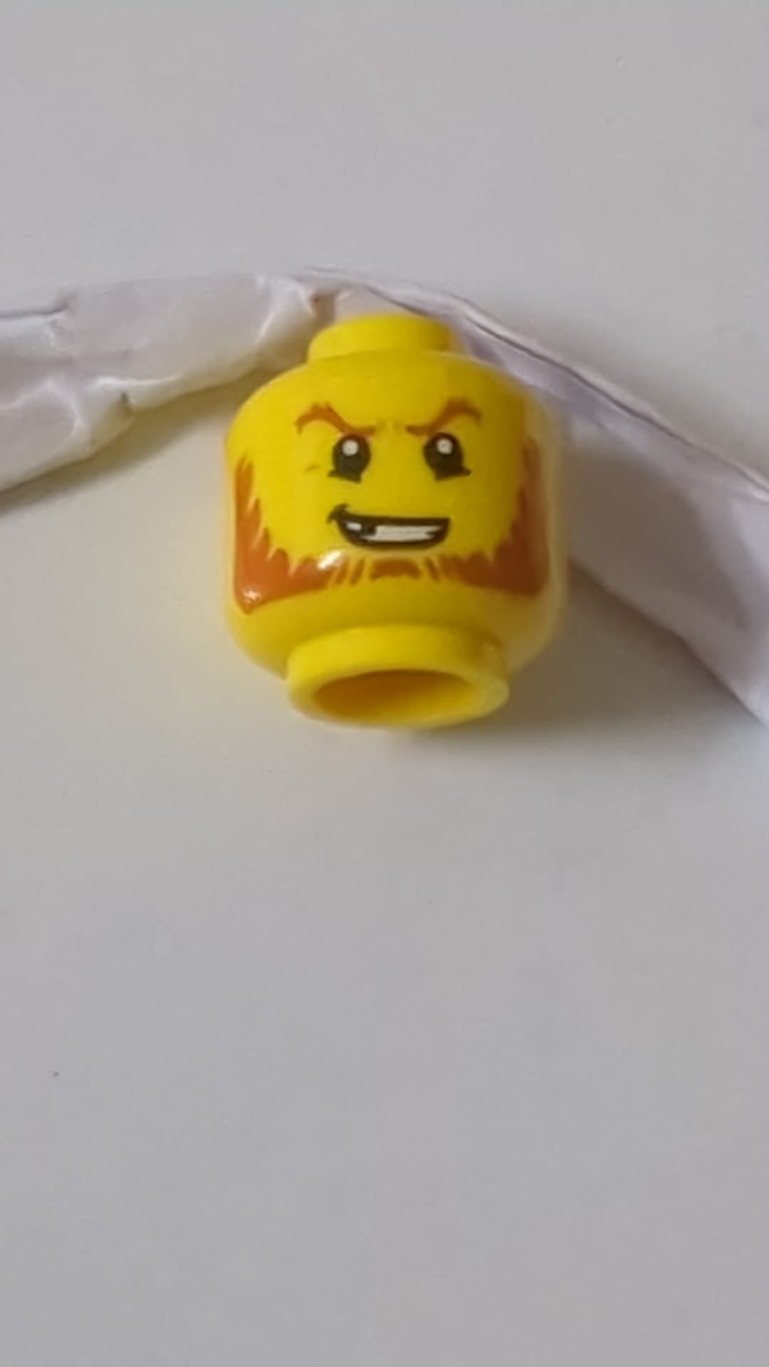 Minifigur, Kopf, dunkelorangefarbene Augenbrauen und Bart, abgebrochener Zahn, entschlossenes Grinsen, Pupillenmuster gelb