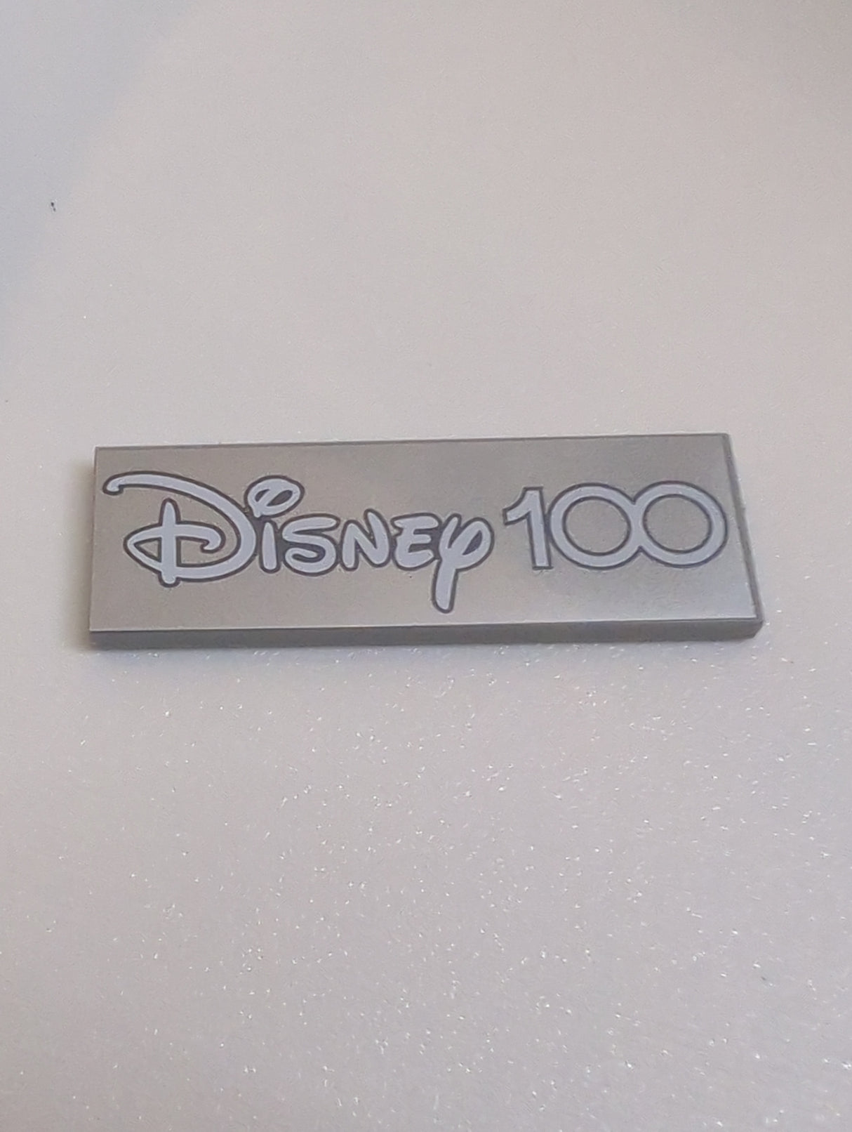 NEU Fliese 2 x 6 mit weißem 'Disney 100' auf silbernem Hintergrundmuster neuhellgrau