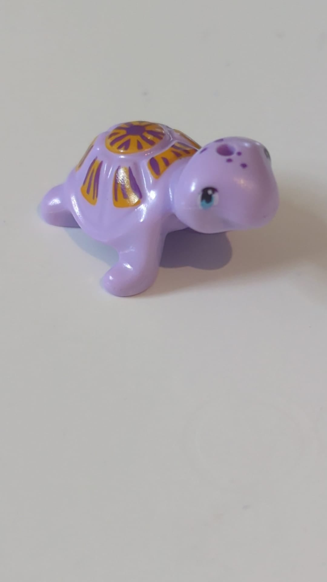 Schildkröte im Mini-Puppenstil mit mittelblauen Augen, dunkelvioletten Flecken und einem hellorangefarbenen Panzer mit Streifenmuster helllavendel