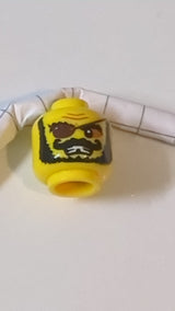 Minifigur, Kopf: Schwarze, buschige Augenbrauen, gezwirbelter Schnurrbart und Bart, dunkelbraune Augenklappe, nougatfarbener Lidschatten, zusammengezogene Stirn, offener Mund mit finsterem Blick und Zähnen, goldenes Muster mit fehlenden Zähnen gelb