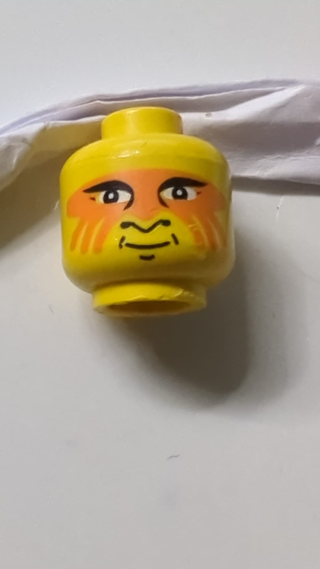 Minifigur, Kopf mit schwarzen Augenlidern, Nasenprofil und Grübchen am Kinn, orangefarbene Gesichtsbemalung, Grinsen gelb