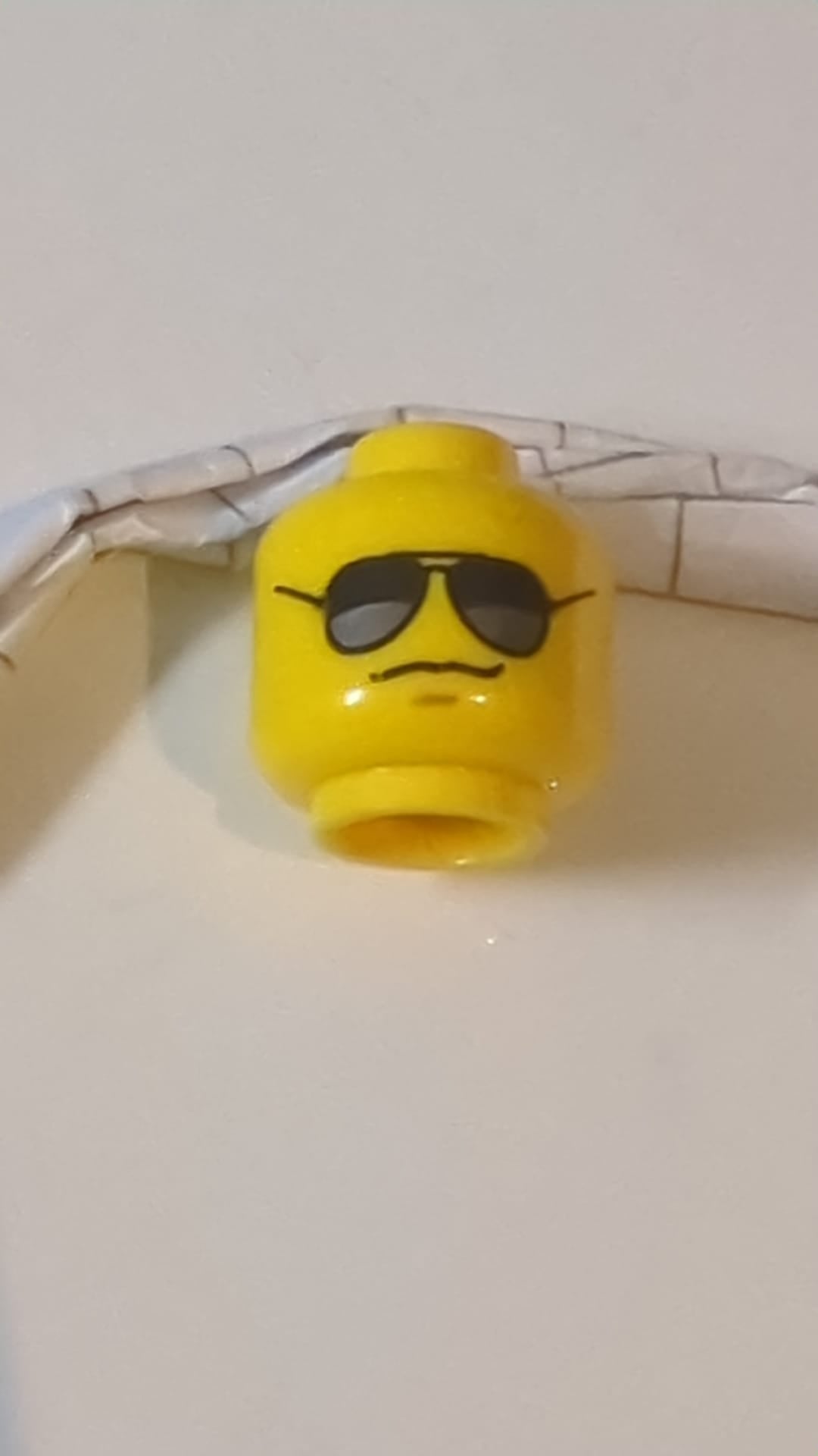 Minifigur, Kopf: Schwarze Sonnenbrille mit dunkelsilbernen Reflexen, mittelgroßes nougatfarbenes Grübchen am Kinn, grimmiges Grinsen gelb