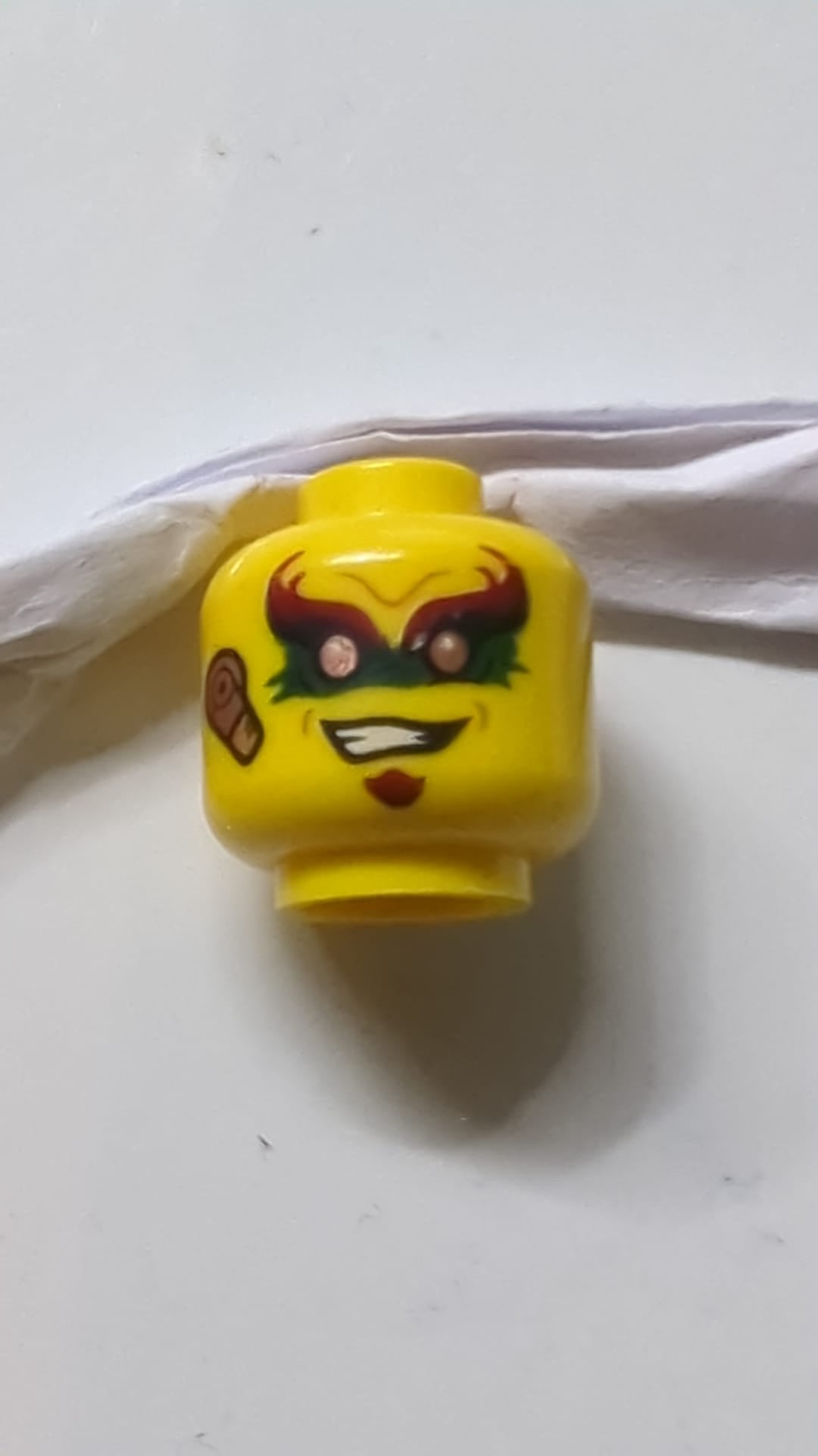 Minifigur, Kopf mit roten Augenbrauen, grüner Augenfarbe, schiefem Lächeln, kupferfarbenem Ohrstückmuster gelb