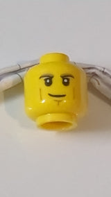 Minifigur, Kopf: Dunkelbraun mit schwarzen Augenbrauen und Oberlidern, mittelbraune Wangenfalten und Grübchen am Kinn, asymmetrisches Grinsen gelb
