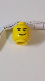 Minifigur, männlicher Kopf mit wütend zusammengezogenen Augenbrauen und finsterem Blick, schwarzes Kinn und Grübchenmuster auf der linken Wange gelb