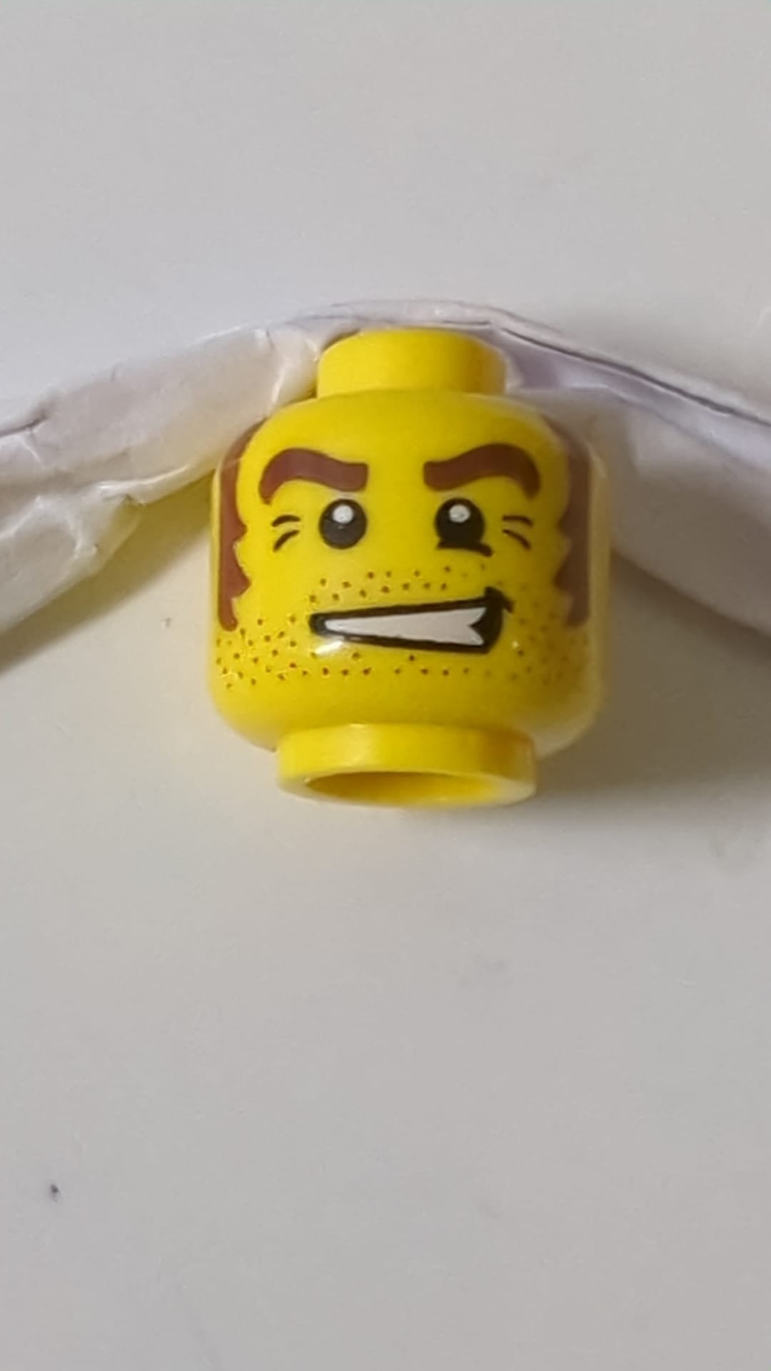 Minifigur, männlicher Kopf mit Bartstoppeln, braunen Augenbrauen und Koteletten, weißen Pupillen gelb