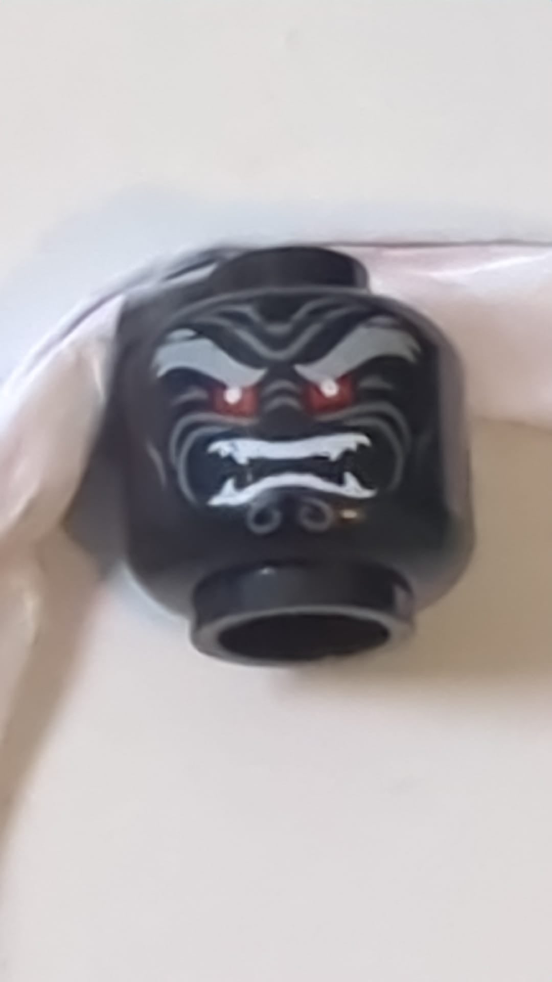 Minifigur, Kopf hellblaugrau, buschige Augenbrauen, rote Augen, dunkelblaugraue Falten, zusammengezogene Stirn, wütend geöffneter Mund mit weißen, spitzen Zähnen, gespaltenes Muster schwarz
