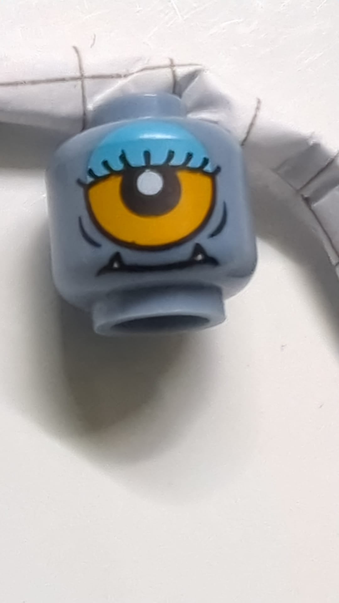 Minifigur, doppelseitiger Alienkopf mit unteren Reißzähnen, Wimpern, einzelnes orangefarbenes Auge offen / Auge halb geschlossen mit blauem Lidschattenmuster sandblau