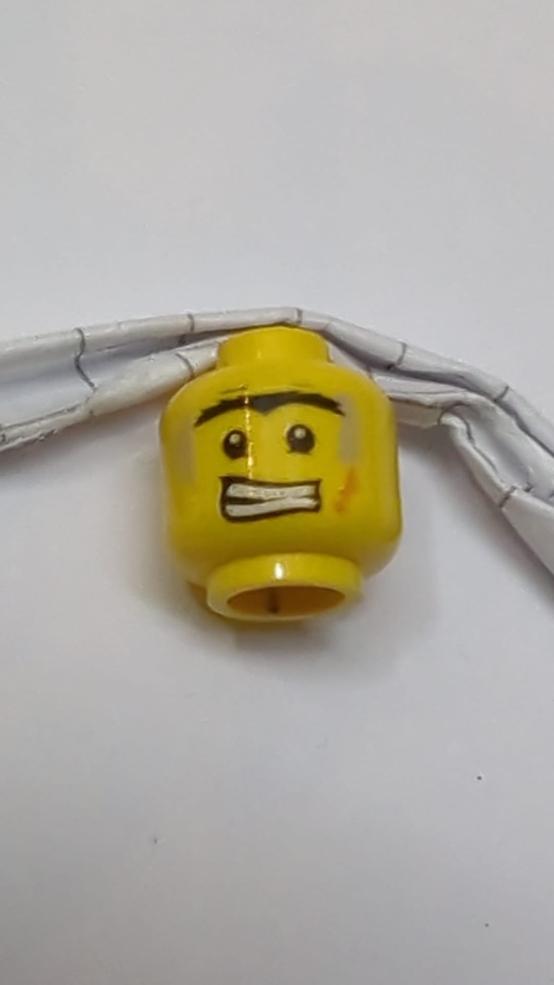 Minifigur, Kopf beidseitig schwarz, buschige Monobraue, Unterlider, hellblaugraue Schmutzflecken, orangefarbene Narbe, wütend gefletschte Zähne / Narbenmuster gelb