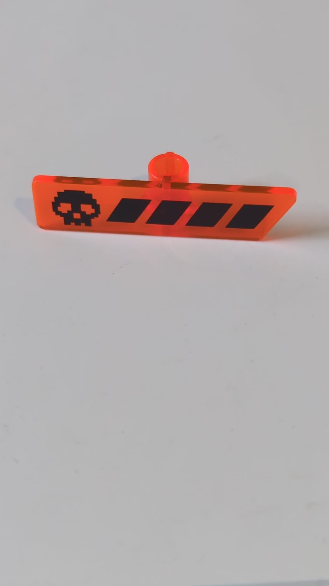 Minifigur, Utensil-Gameplayer-Etikett mit pixeligem schwarzem Totenkopf und unterbrochenem Streifen-/Gesundheitsbalkenmuster transparent neonorange