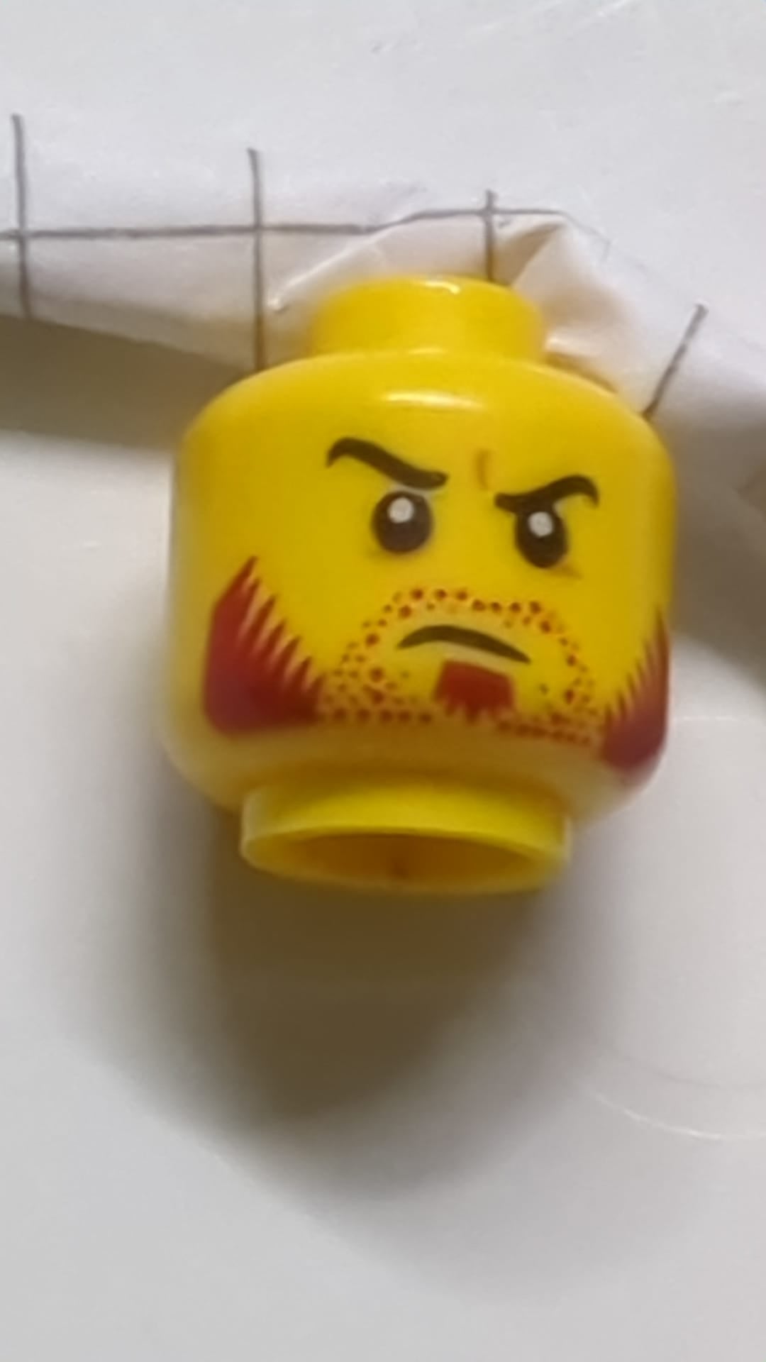 Minifigur, Kopf mit doppelseitigem Bartstoppeln, dunkelroten Koteletten, Spitzbart, geschwungenen schwarzen Augenbrauen, schiefem, offenem Grinsen / entschlossenem Gesichtsausdruck gelb