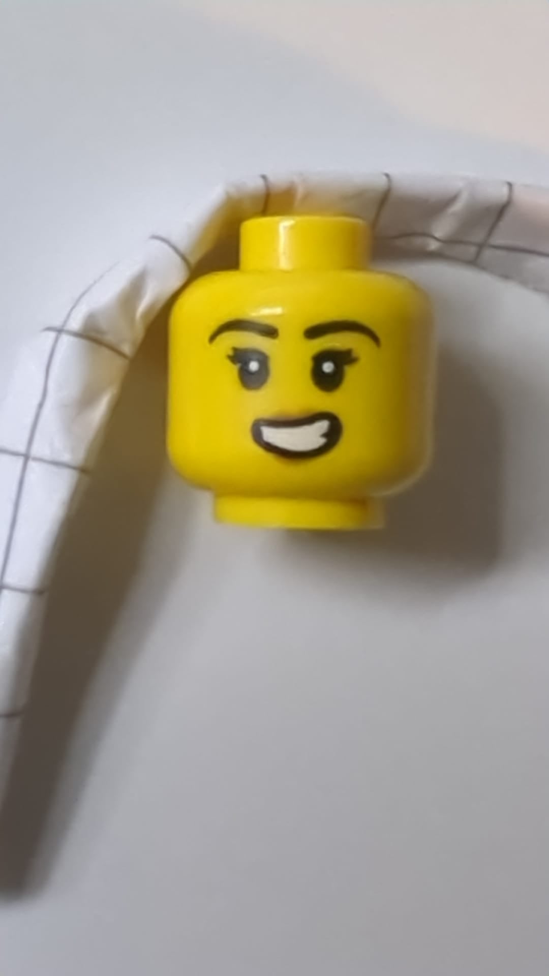 Minifigur, weiblicher Kopf, schwarze Augenbrauen, doppelte Wimpern, mittelbraune Lippen, schiefes, offenes Lächeln mit Zahnmuster gelb