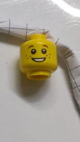 Minifigur, Kopf: Kind, kleine rötlich-braune, weit auseinanderstehende Augenbrauen, Sommersprossen, offener Mund mit Lächeln und sichtbaren Zähnen gelb